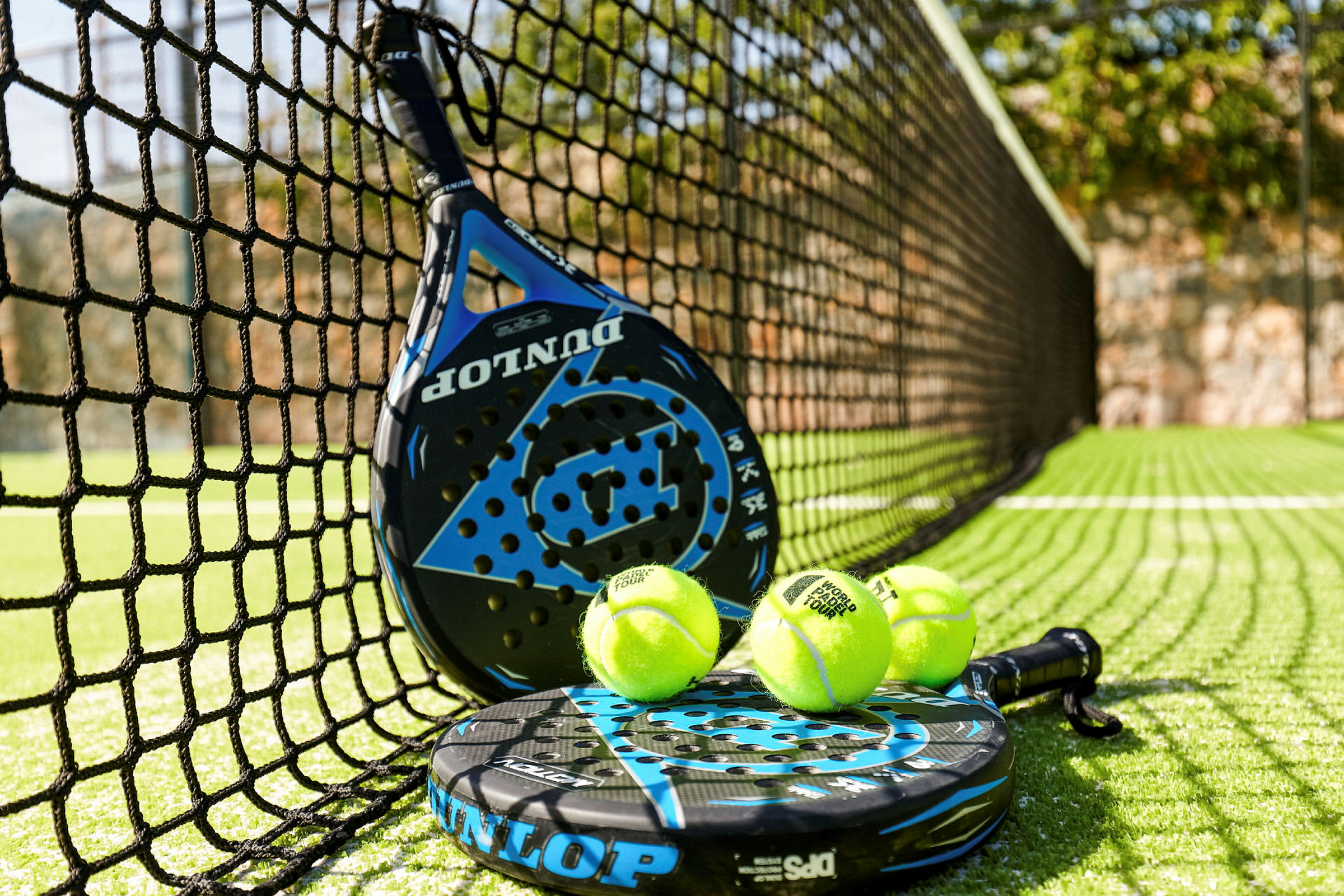 En padelracket och padelbollar vid nätet på en padelbana. (AI-genererad text)
