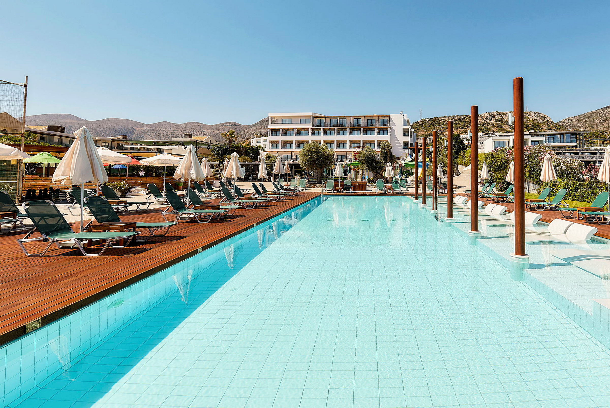 Poolområde med solstolar och parasoller bredvid ett hotell. (AI-genererad text)