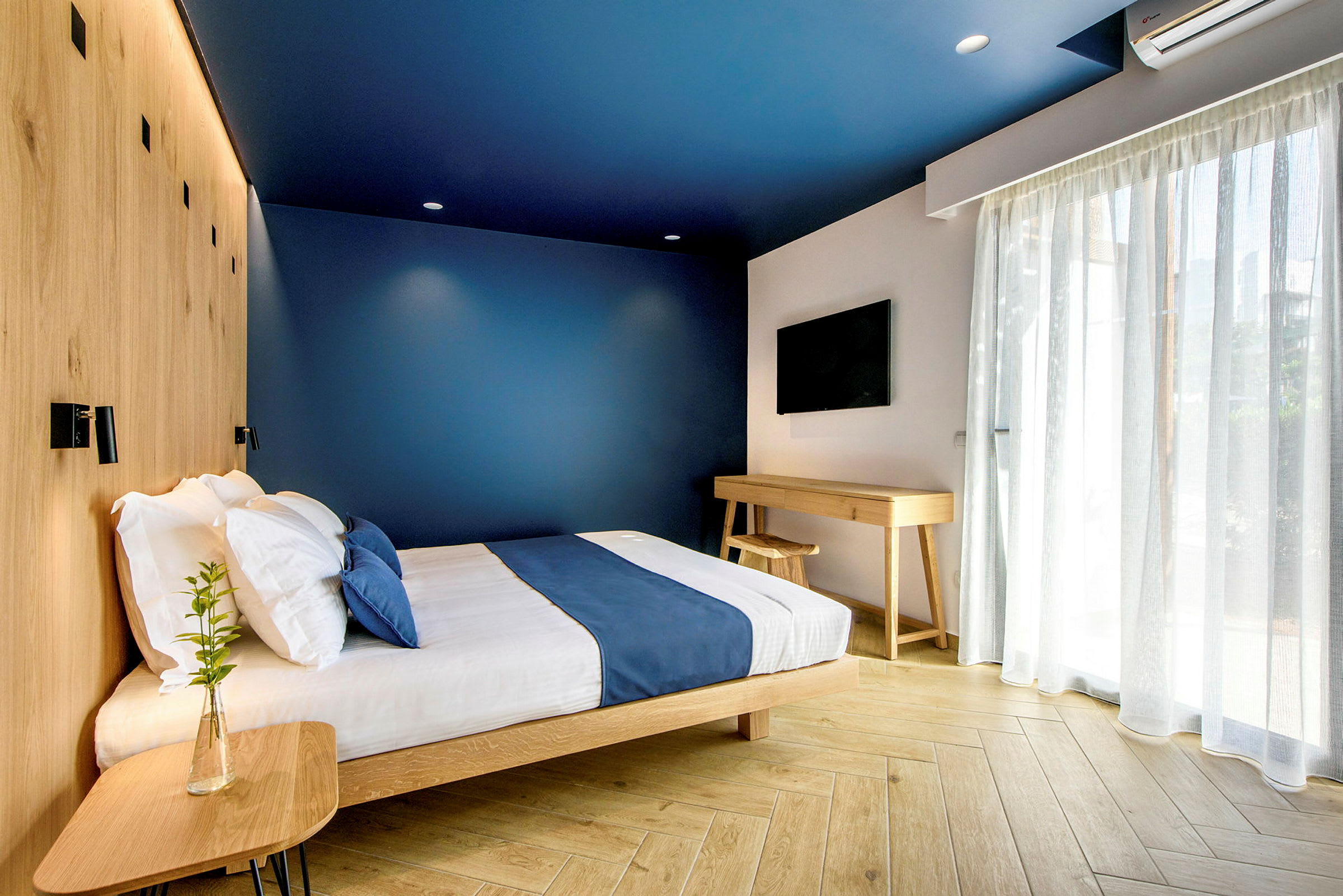 Ett modernt hotellrum med blå väggar, en säng med blå överkast och träinredning. (AI-genererad text)