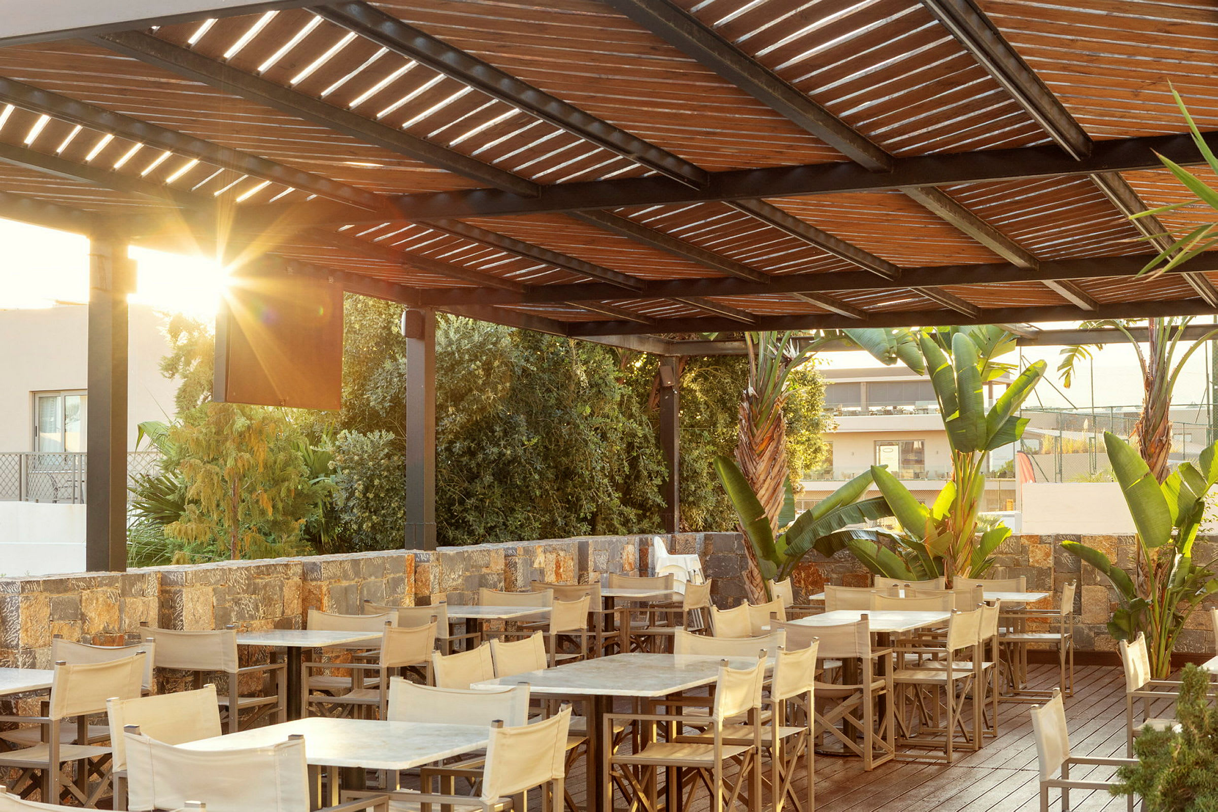 En uterestaurang med bord, stolar, träpergola och omgivande växtlighet. (AI-genererad text)