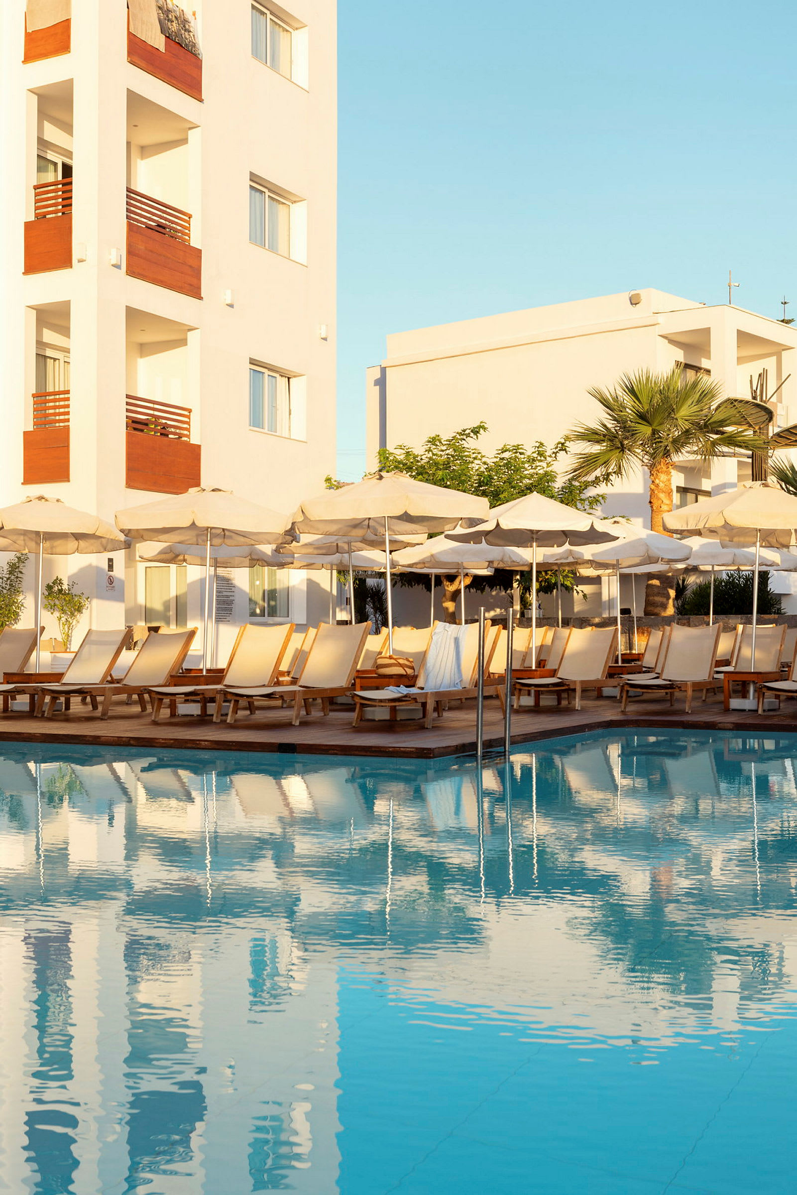 Bild av en pool med solstolar och parasoller samt en byggnad i bakgrunden. (AI-genererad text)