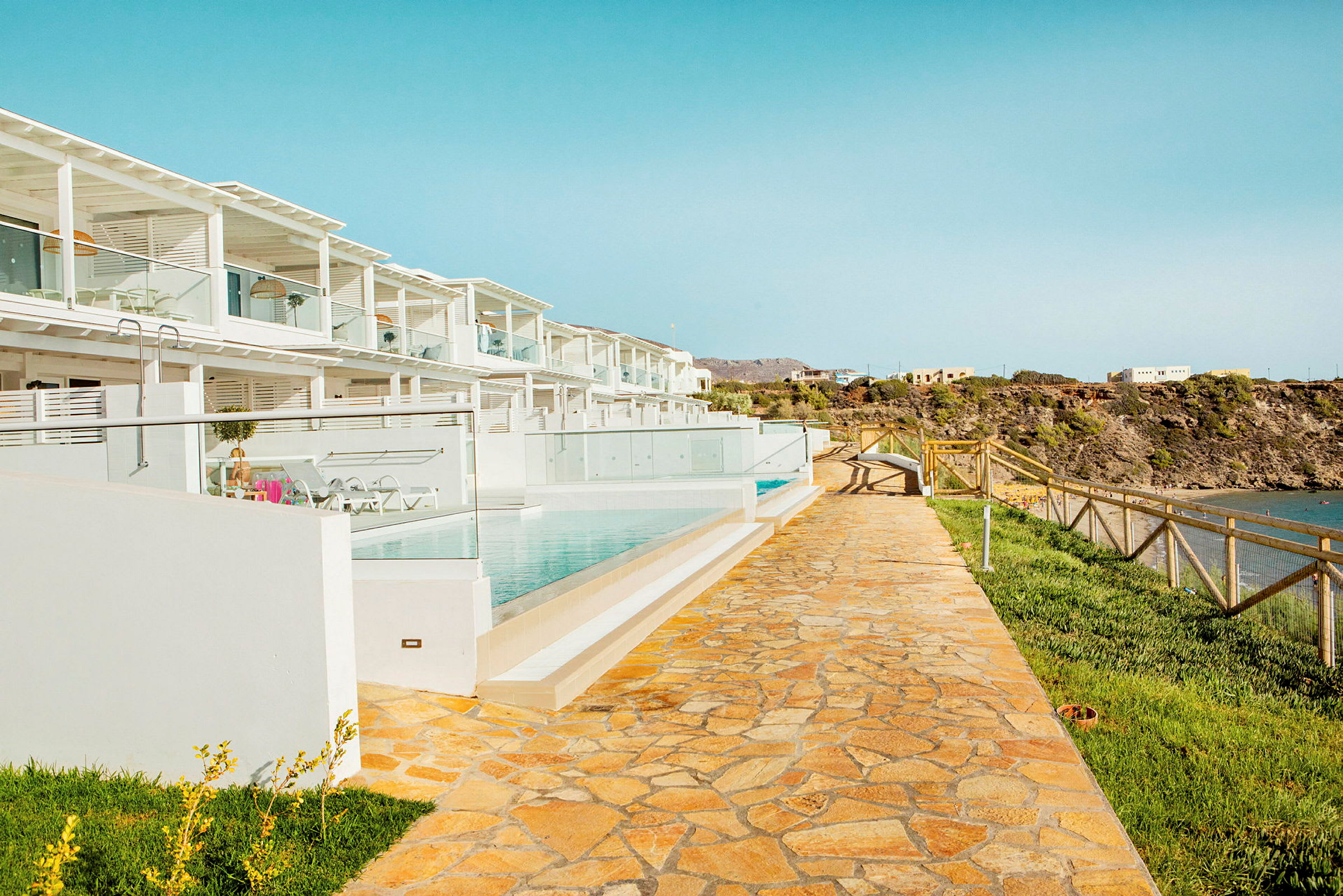 Bild av en modern resort med vit arkitektur, en gångväg, pooler och utsikt mot kusten. (AI-genererad text)