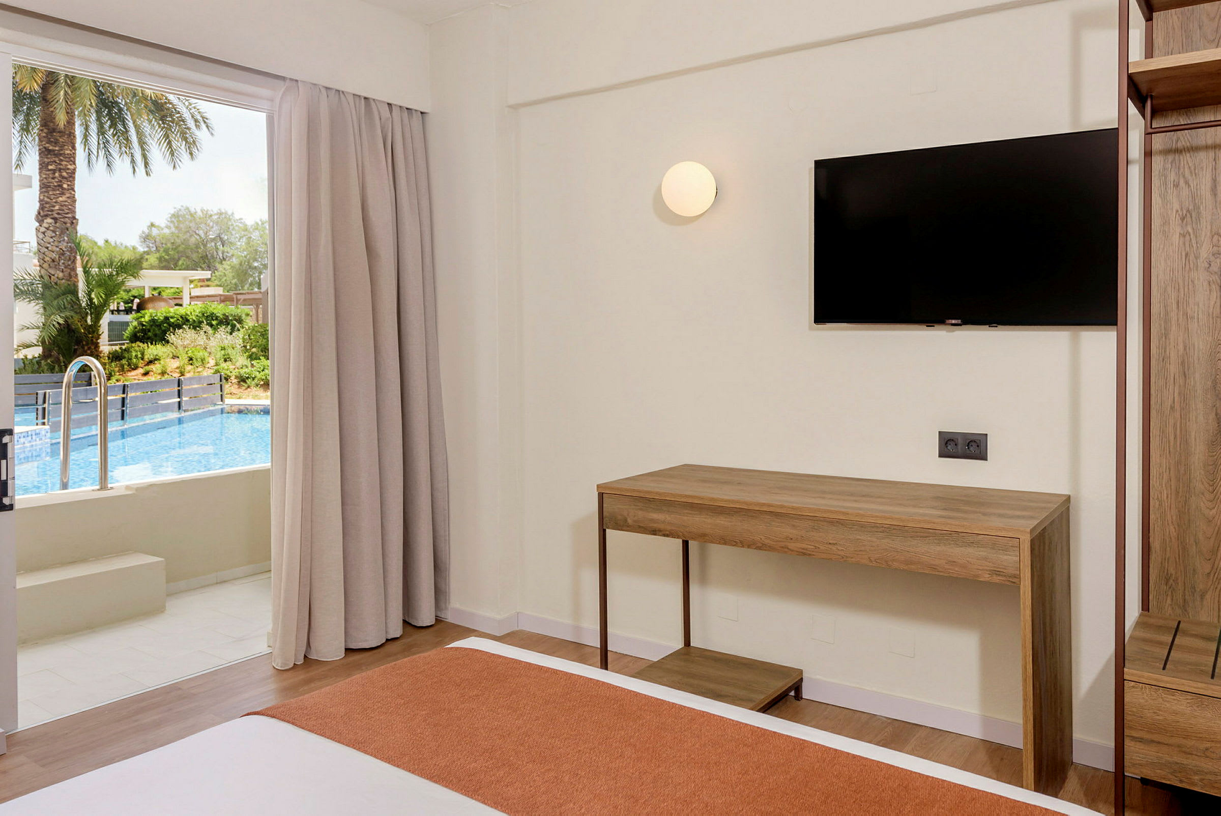 Bild av ett hotellrum med säng, skrivbord och en TV på väggen. En glasdörr öppnar ut till en pool och en palm i bakgrunden. (AI-genererad text)
