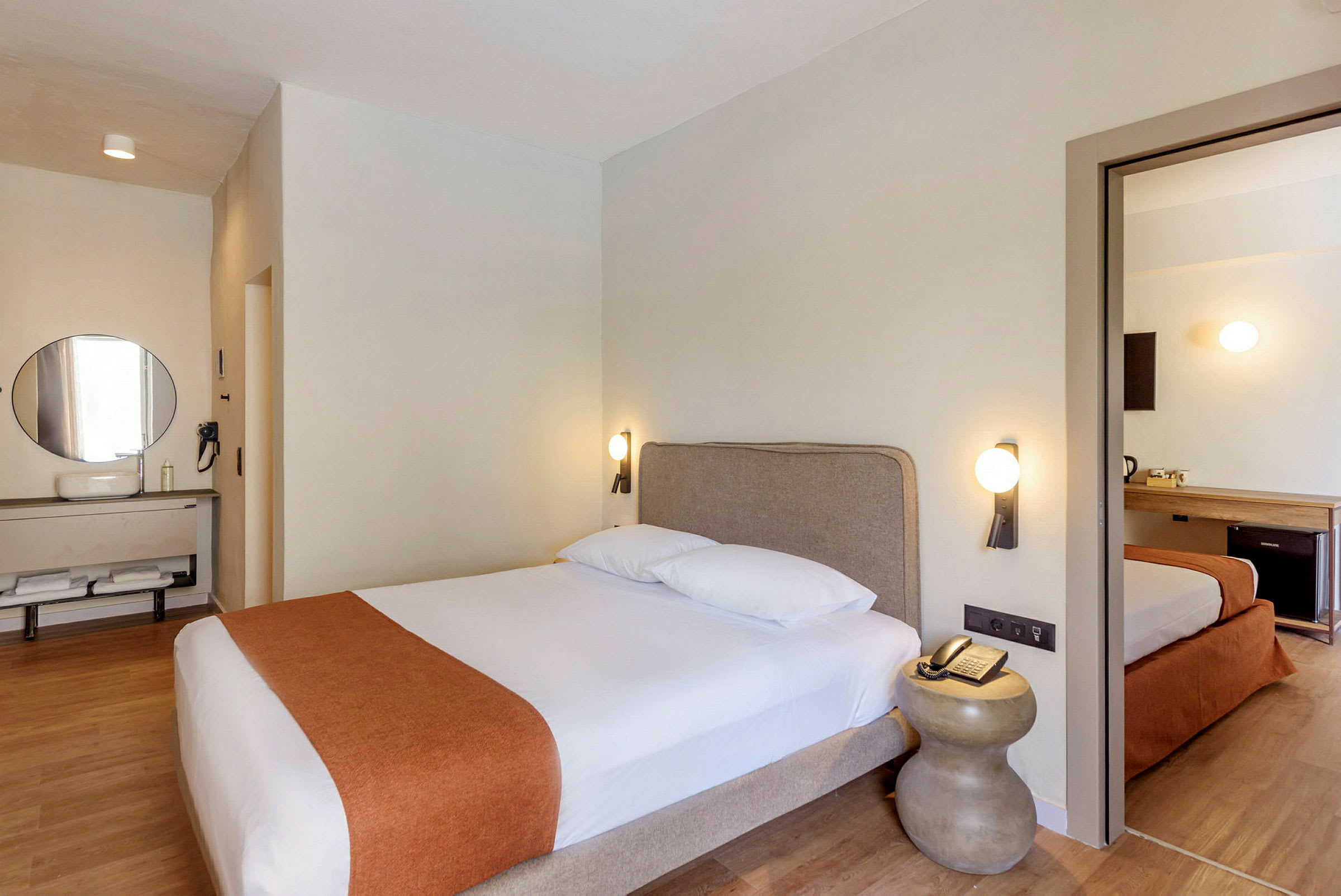 Ett hotellrum med en dubbelsäng, ett nattduksbord och en spegel ovanför ett handfat. (AI-genererad text)