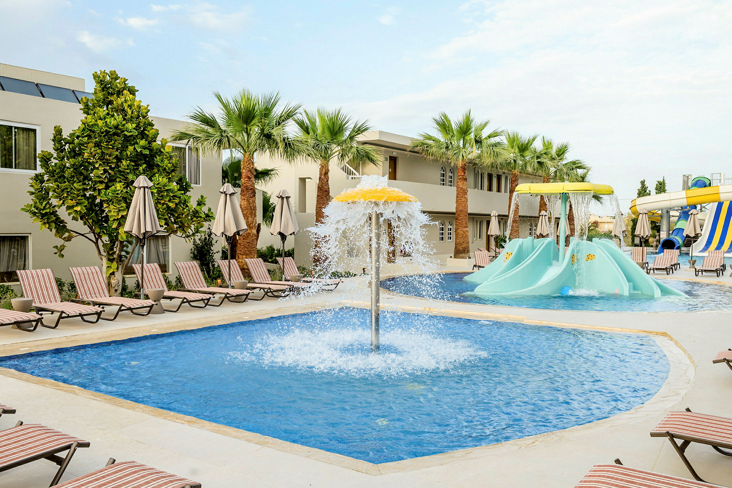En pool med vattenfontän och barnbilder på ett hotellområde. (AI-genererad text)