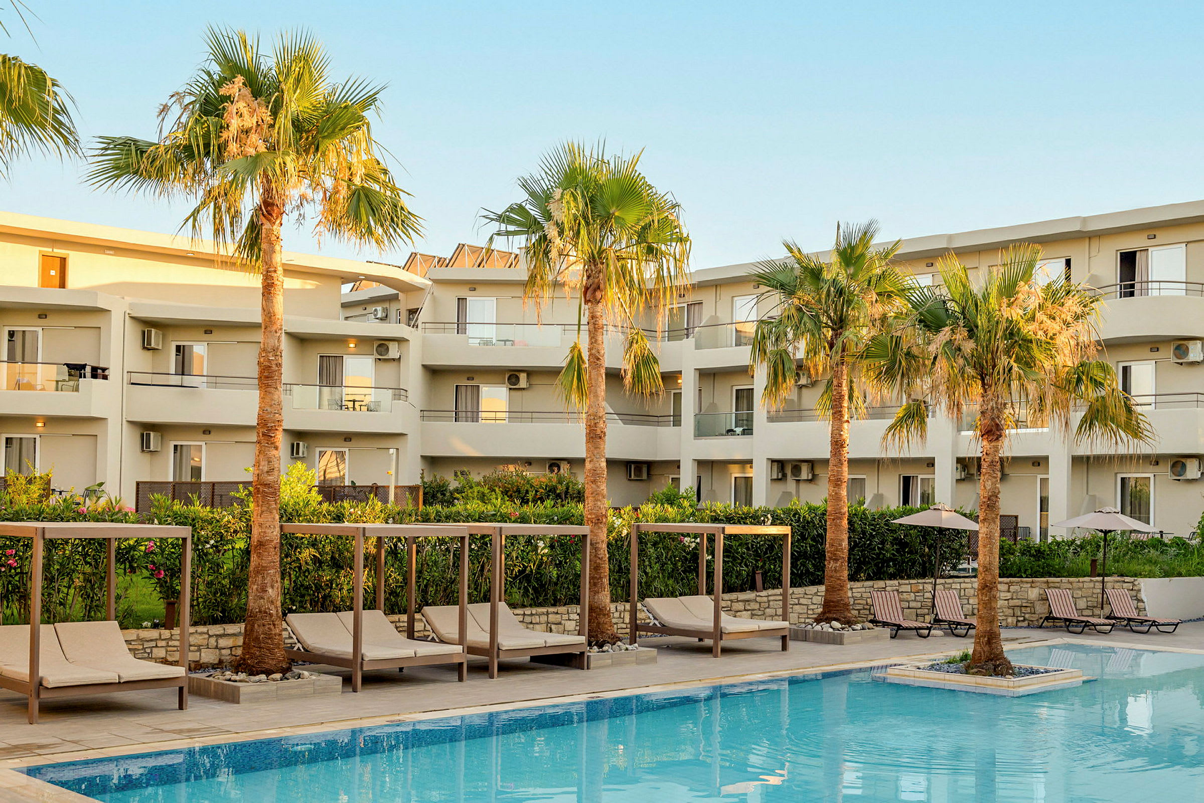 Hotellbyggnad med pool i förgrunden och solstolar samt parasoller vid sidan. (AI-genererad text)