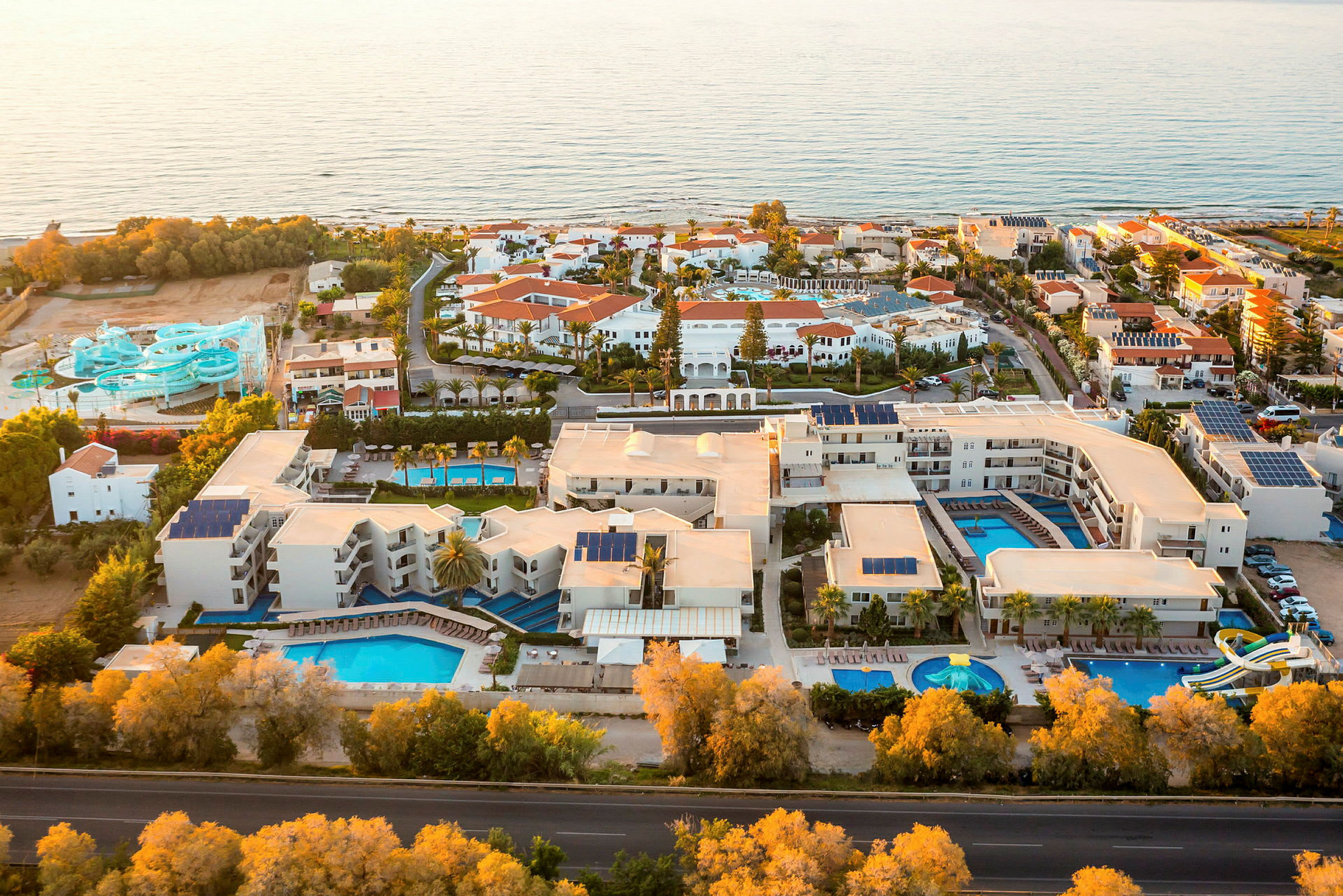 Flygvy över ett semesterhotell med flera pooler och vattenrutschkanor vid havet. (AI-genererad text)