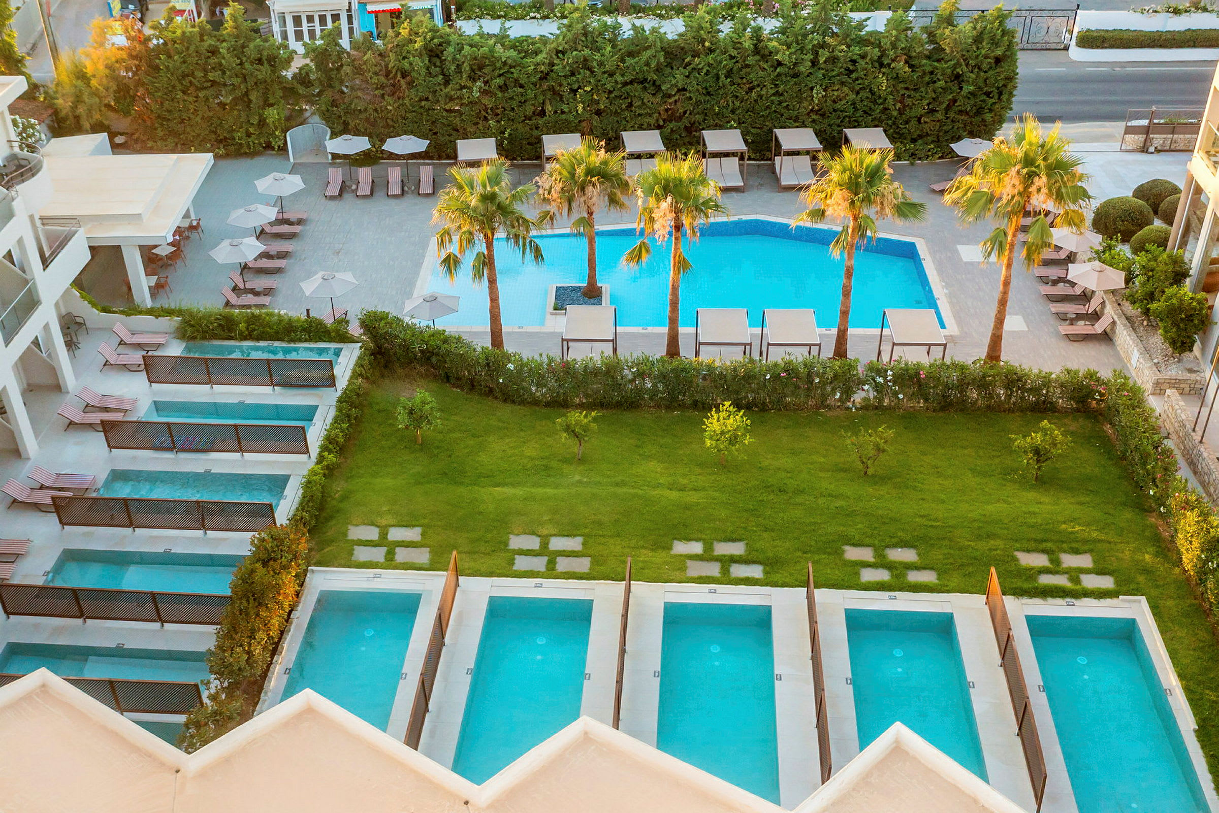 En vy över ett hotellområde med flera privata små pooler och en större pool omgiven av solstolar och parasoller. (AI-genererad text)