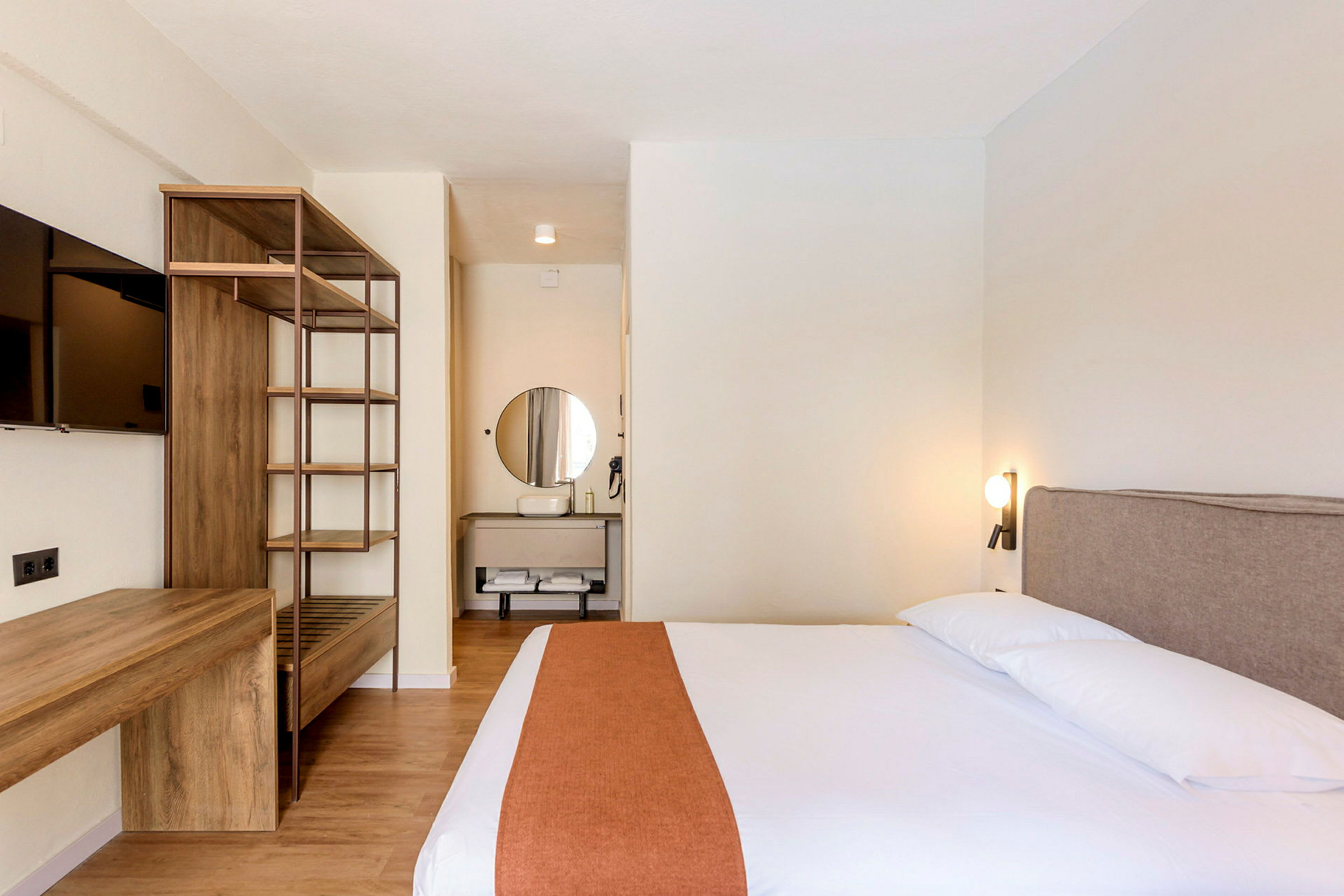 Ett hotellrum med en säng, en öppen garderob och en tv på väggen. (AI-genererad text)