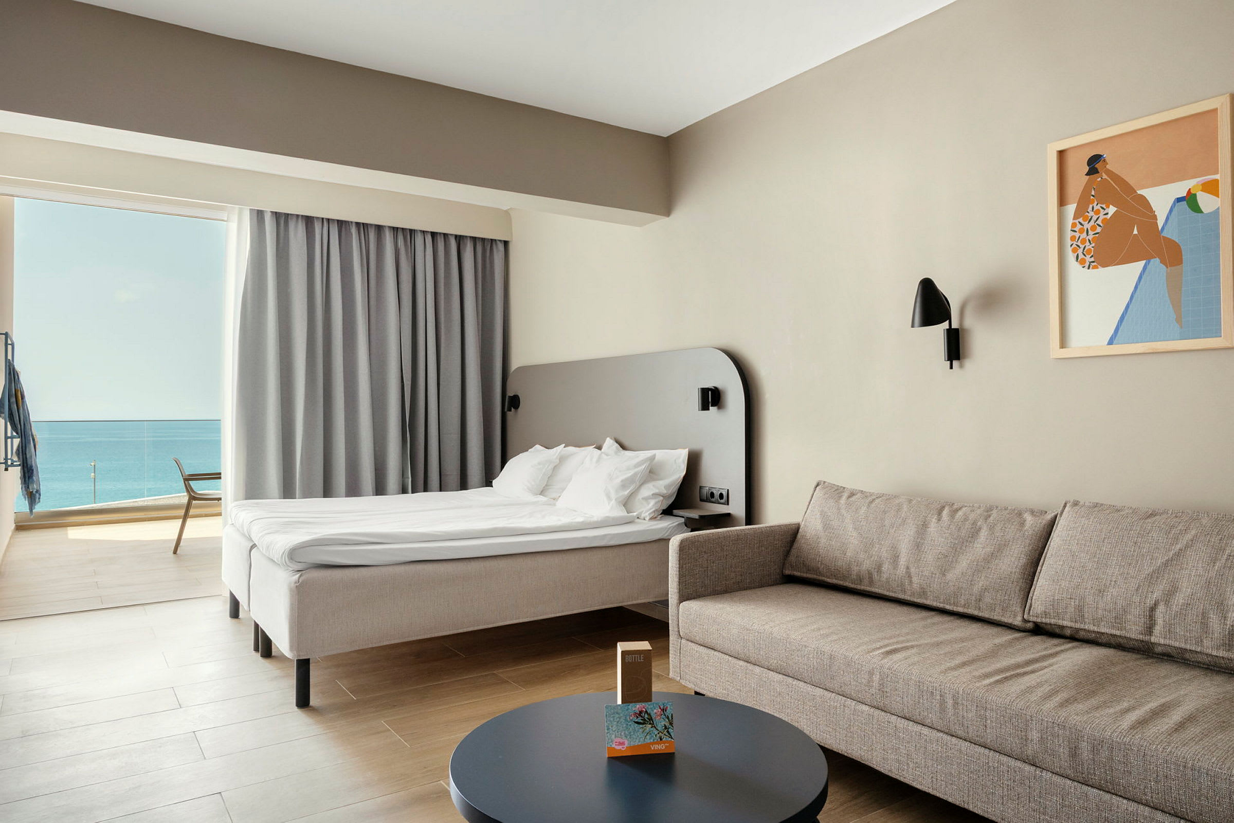 En hotelldeluxe-rum med ljus inredning, en bekväm soffa, bord, och en säng med utsikt över havet. (AI-genererad text)