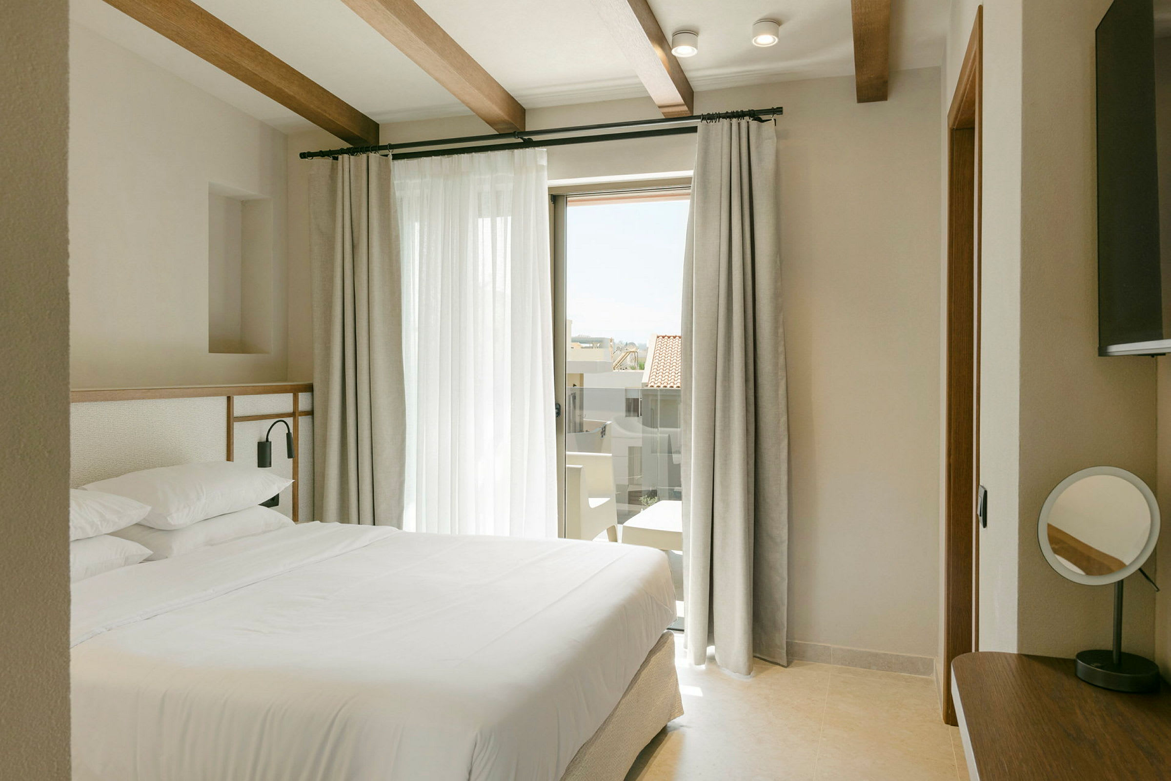 Ett modernt hotellrum med en stor säng, ljusa gardiner och en glasdörr som leder till en balkong. (AI-genererad text)