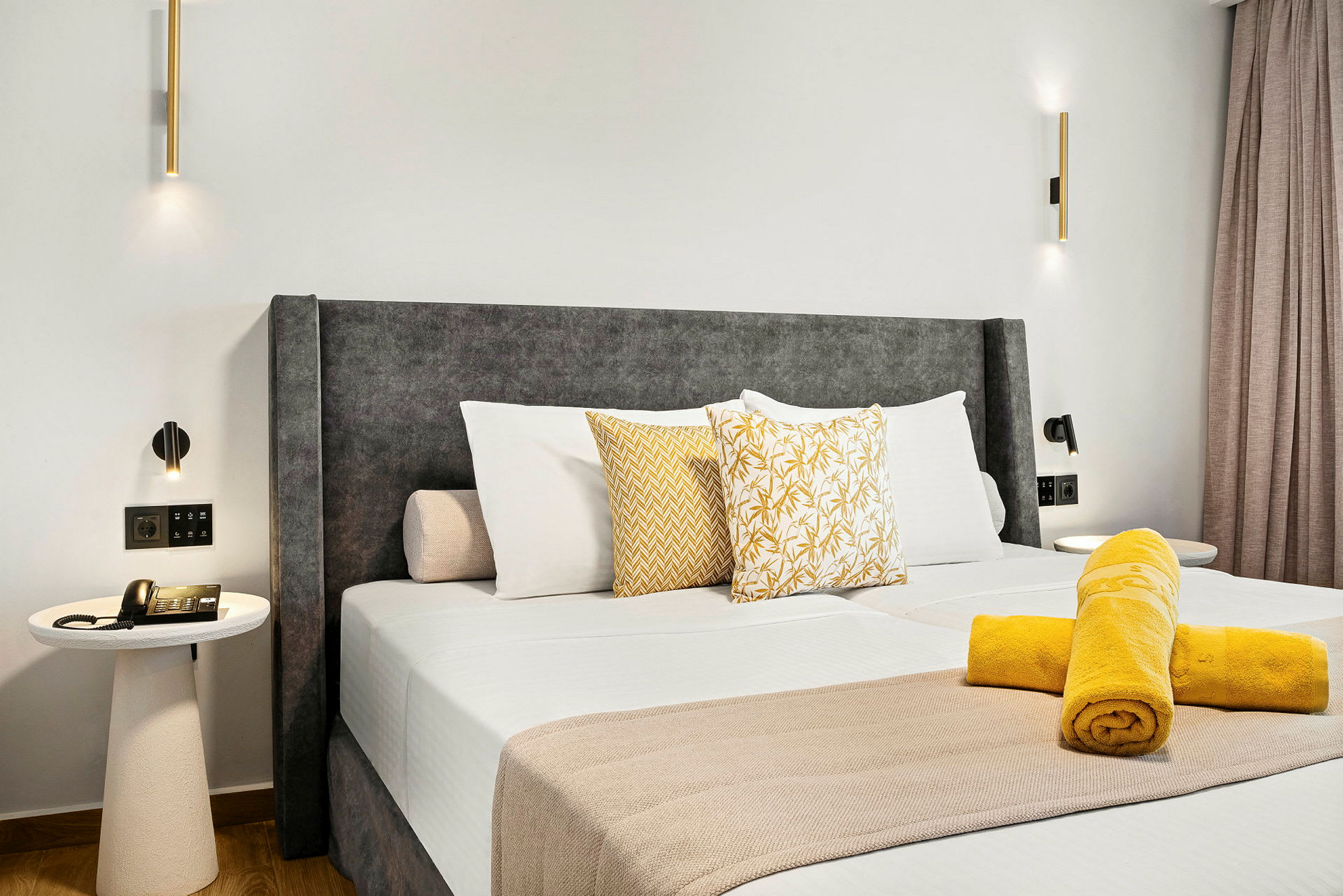 Ett hotellrum med en stor säng, prydd med kuddar och hoprullade handdukar på täcket. Bord med telefon syns bredvid sängen. (AI-genererad text)