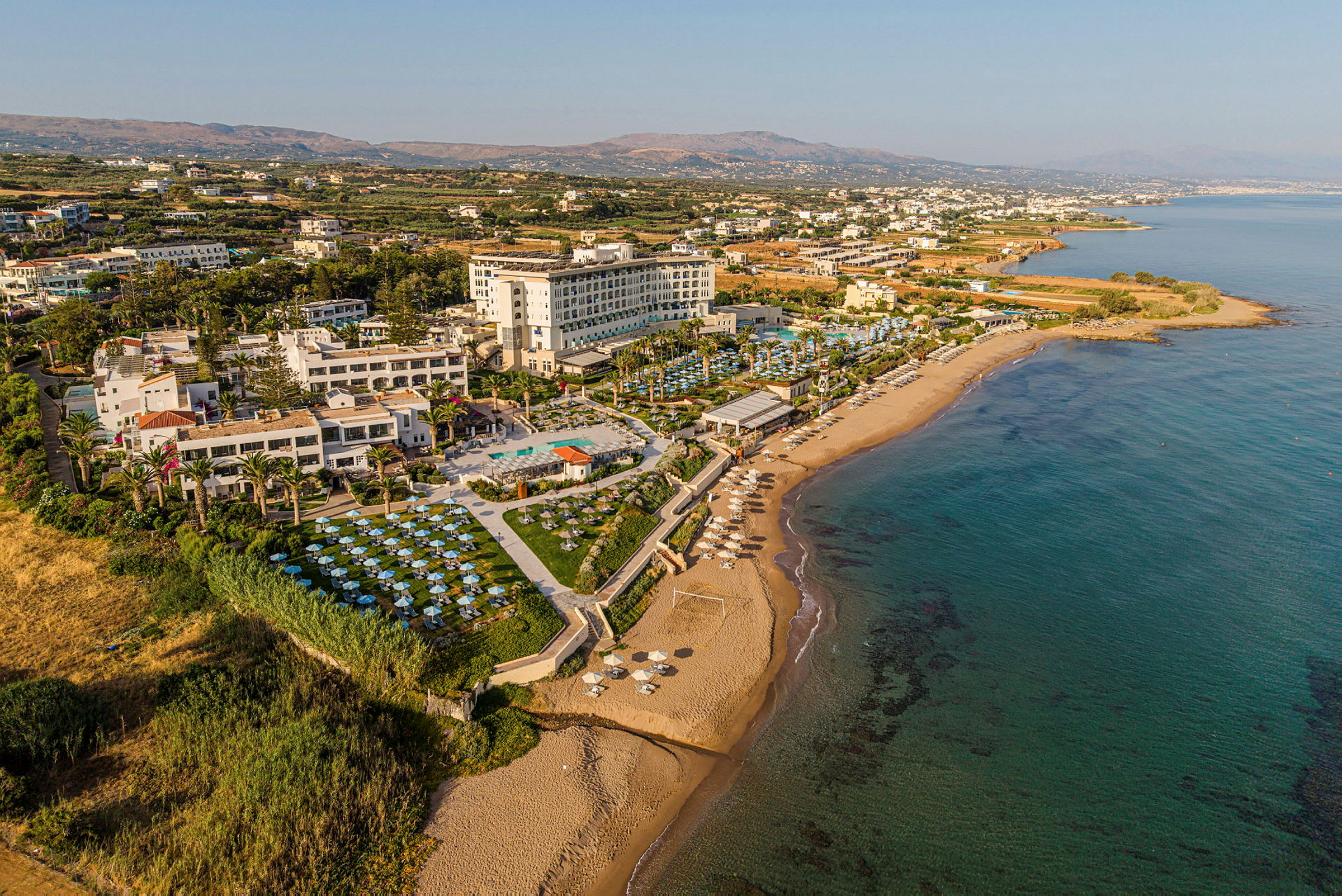 Bild av kustnära semesterort med hotellkomplex, pooler och solstolar vid stranden. (AI-genererad text)