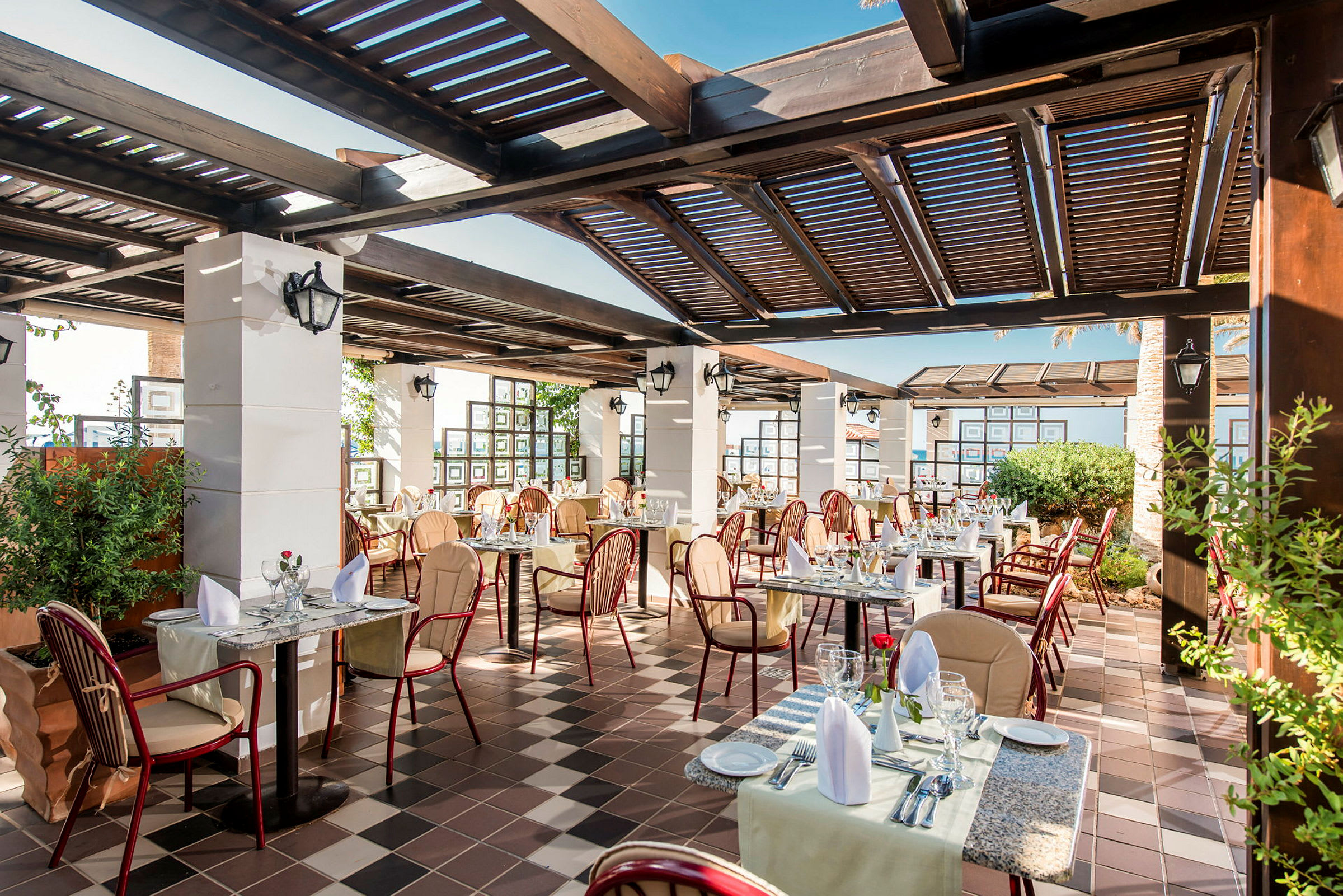 En utomhusrestaurang med dukade bord och stolar under en pergola. (AI-genererad text)