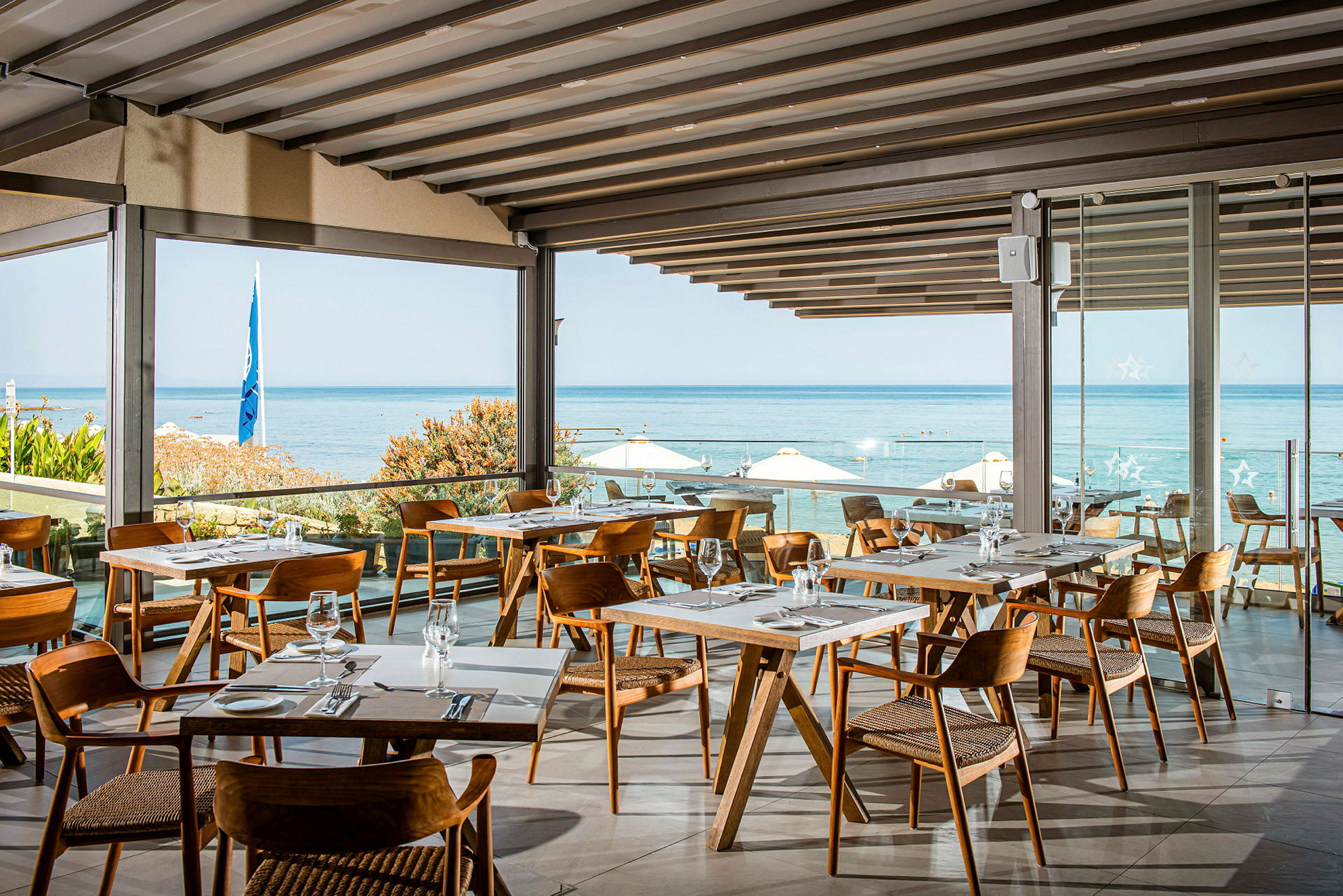 Restaurang med moderna träbord och stolar, med utsikt över havet och stranden. (AI-genererad text)