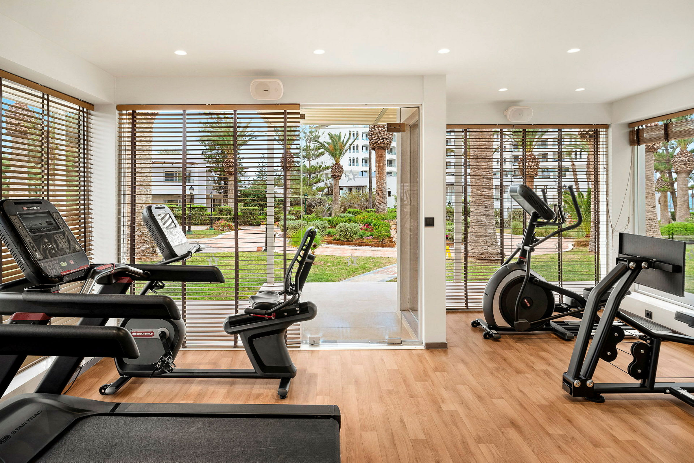 Ett gym med träningsutrustning och stora fönster som vetter mot en grönskande trädgård. (AI-genererad text)