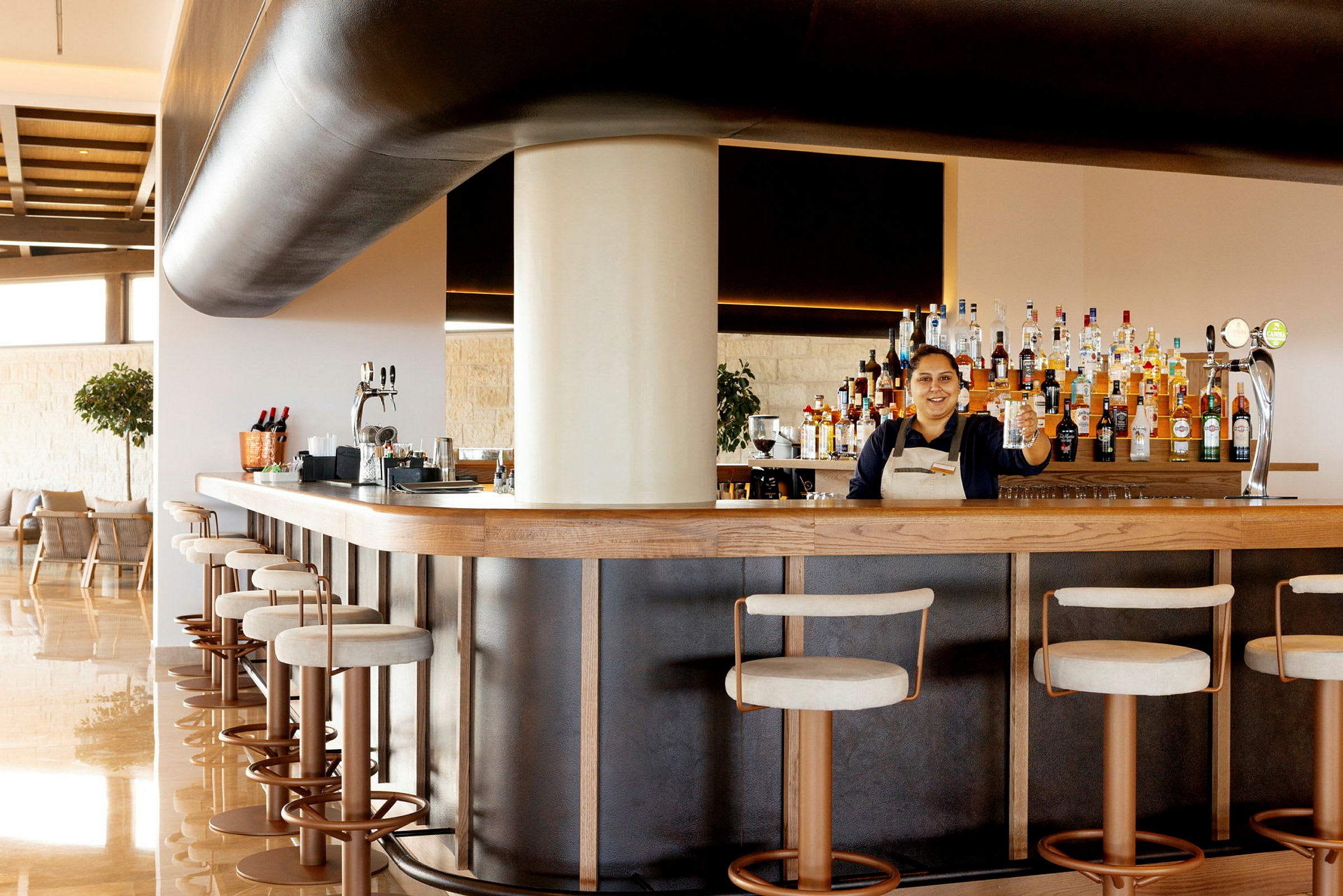 En bartender står bakom en välutrustad bar med barstolar framför. (AI-genererad text)