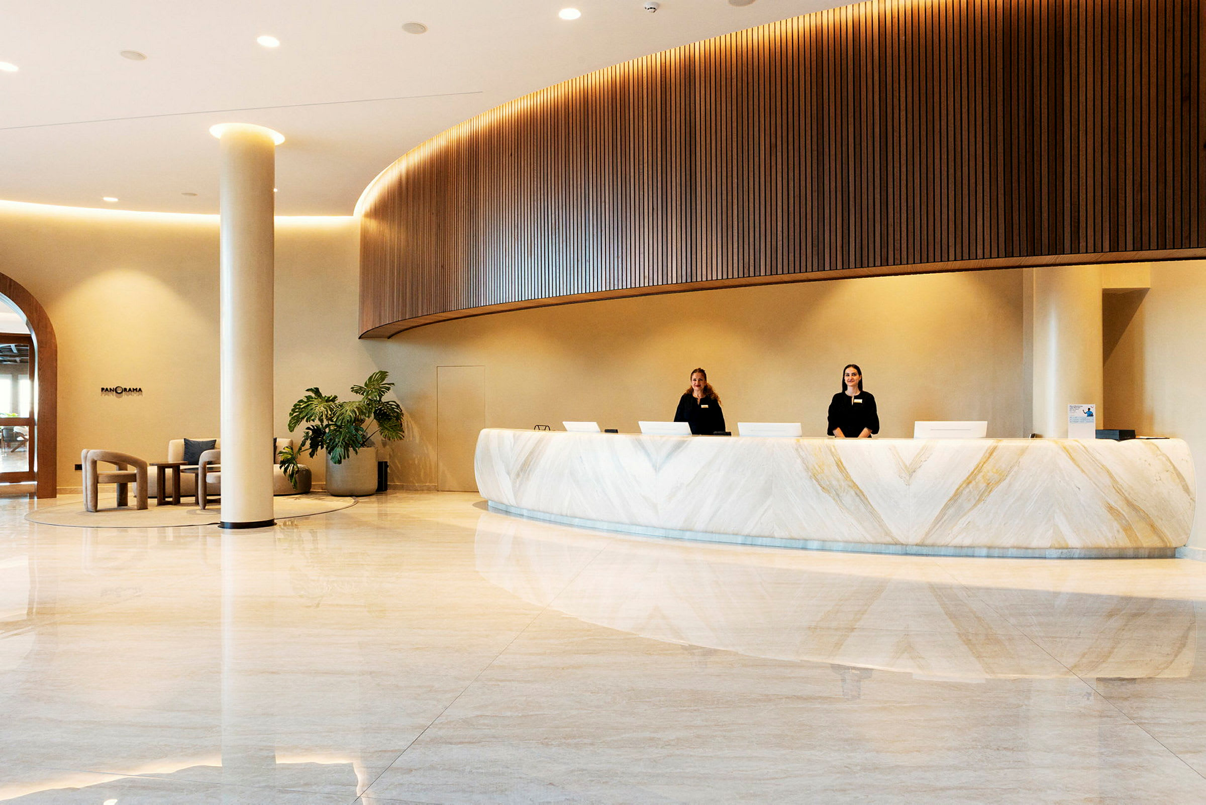 Bild av en hotellreception med en modern inredning, där två receptionister står bakom en vit marmorerad disk. (AI-genererad text)