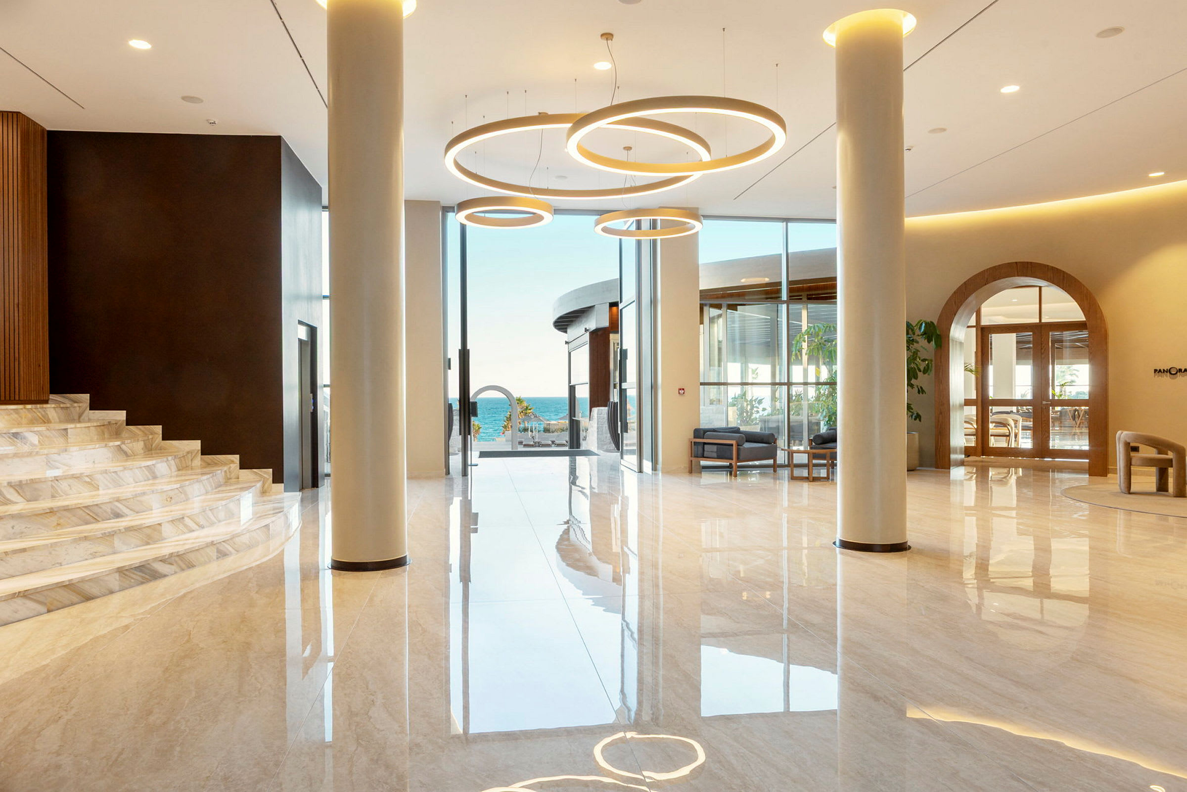 Ljus och modern lobby med stora glaspartier och utsikt mot havet samt eleganta armaturer i taket. (AI-genererad text)