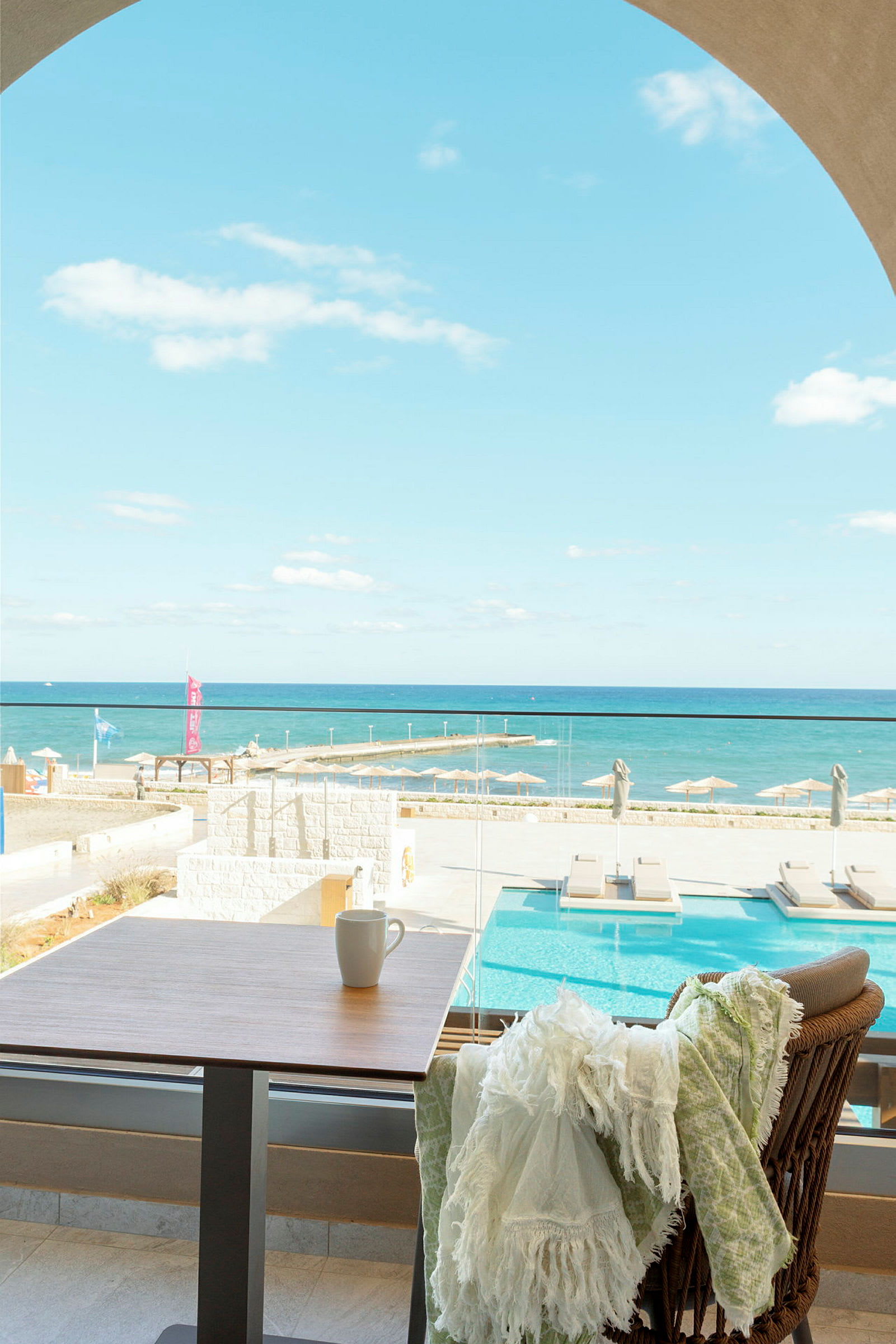 Utsikt över en pool och havet från en terrass, med ett bord och en stol i förgrunden. (AI-genererad text)