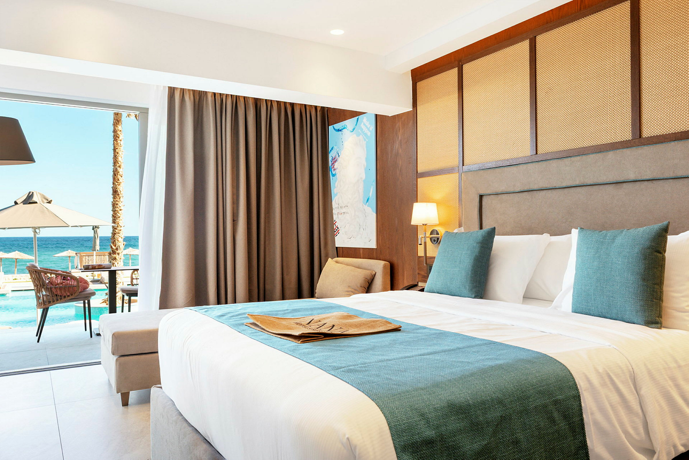 Ett hotellrum med en stor säng, dekorerad med kuddar och en filt. Rummet har glasdörrar som leder ut till en balkong med utsikt över en pool och havet. (AI-genererad text)