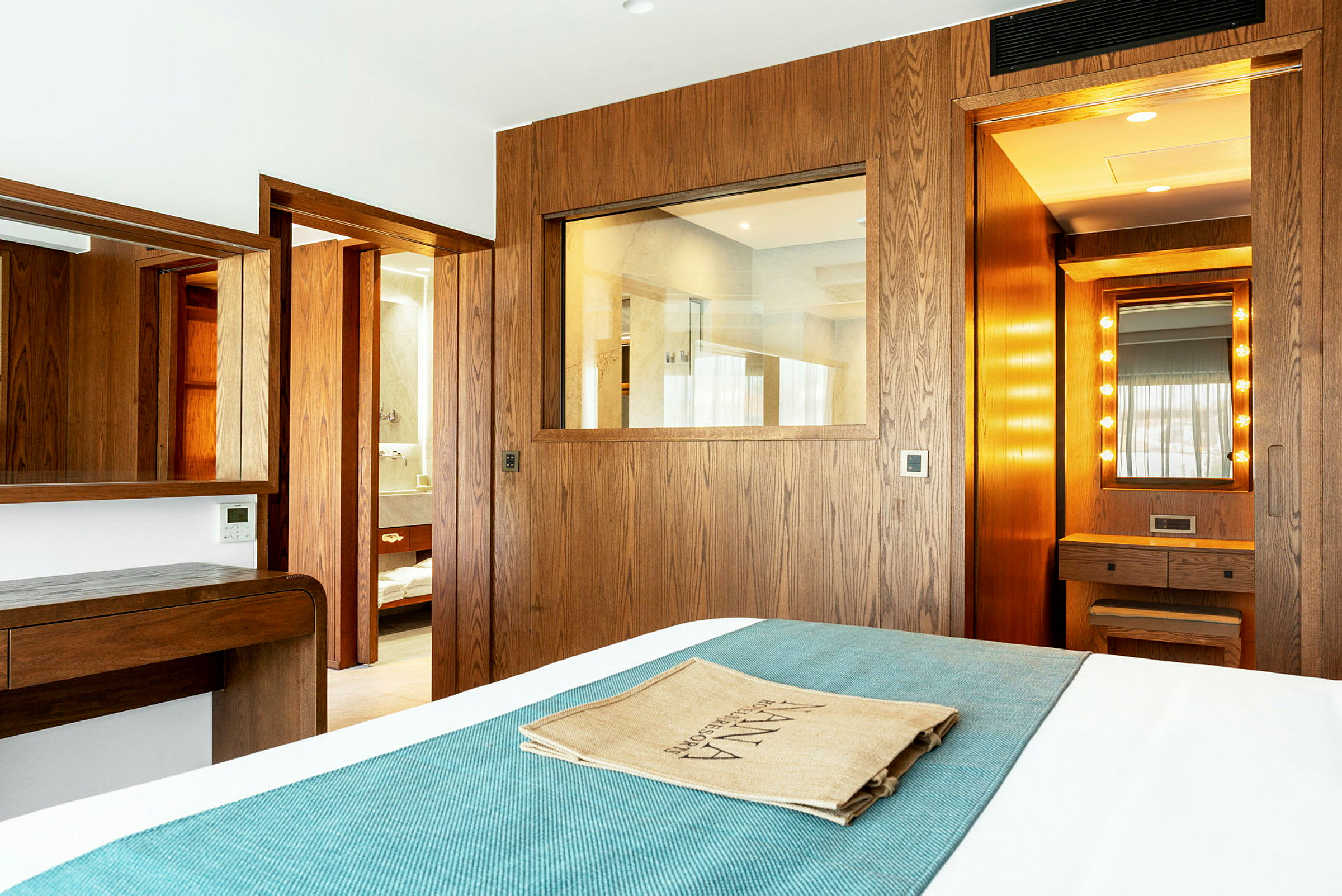 Ett hotellrum med träinredning, spegel och ett sängöverkast i turkost. (AI-genererad text)