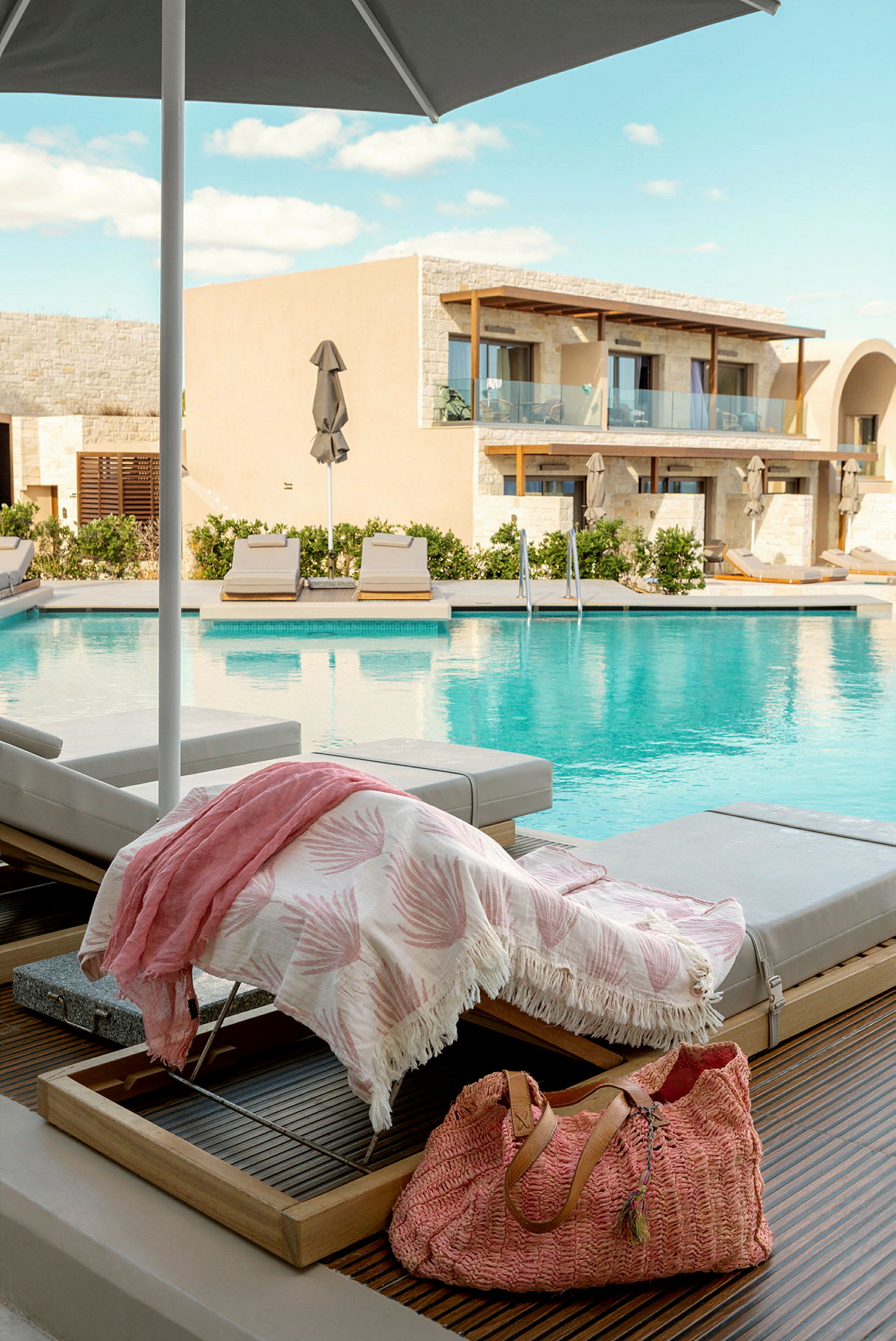 Bild föreställer en pool med solstolar, en handduk och en väska i förgrunden. Bakom syns byggnader med balkonger. (AI-genererad text)