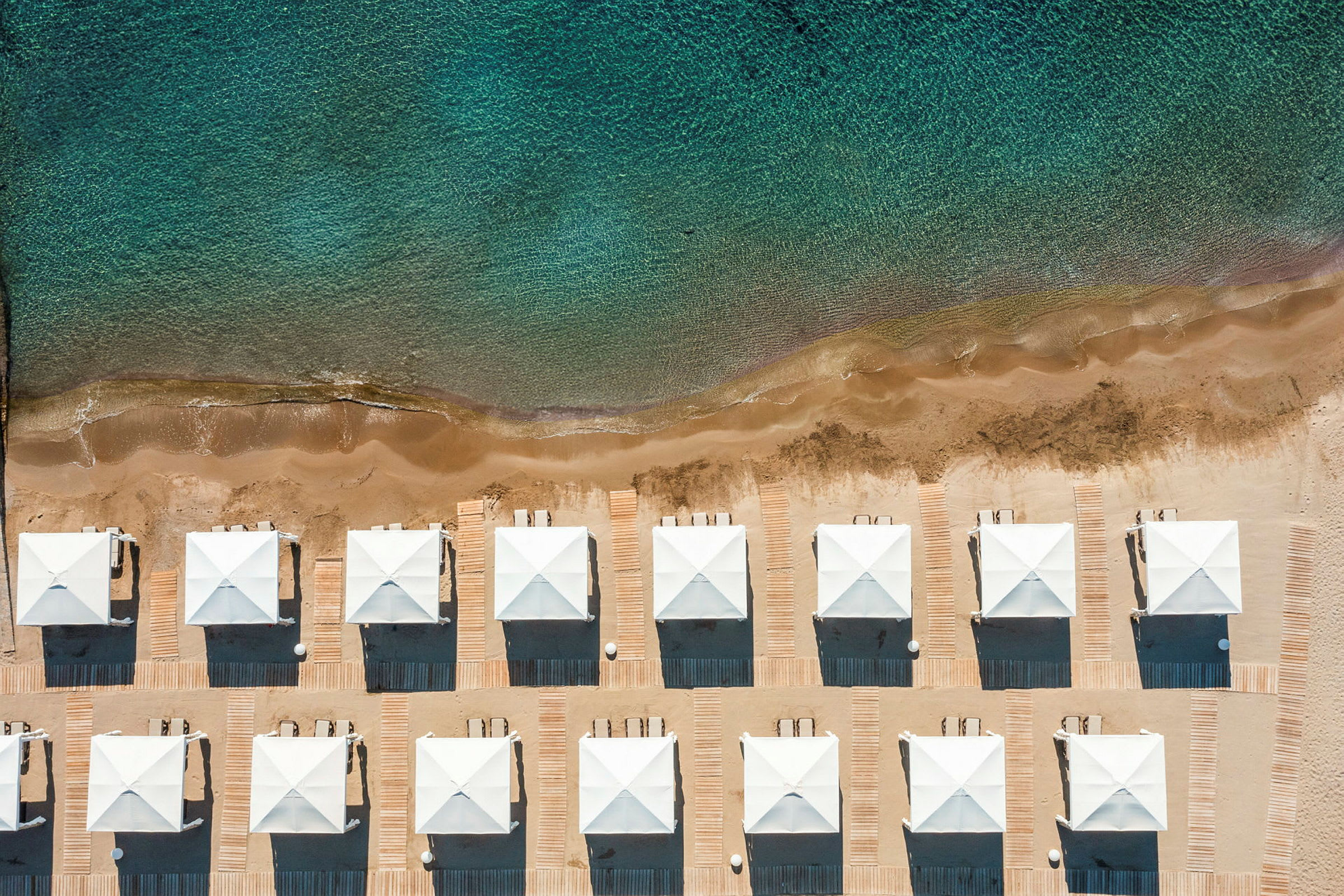 Bilden visar en rad vita strandpaviljonger på en sandstrand vid havet. (AI-genererad text)