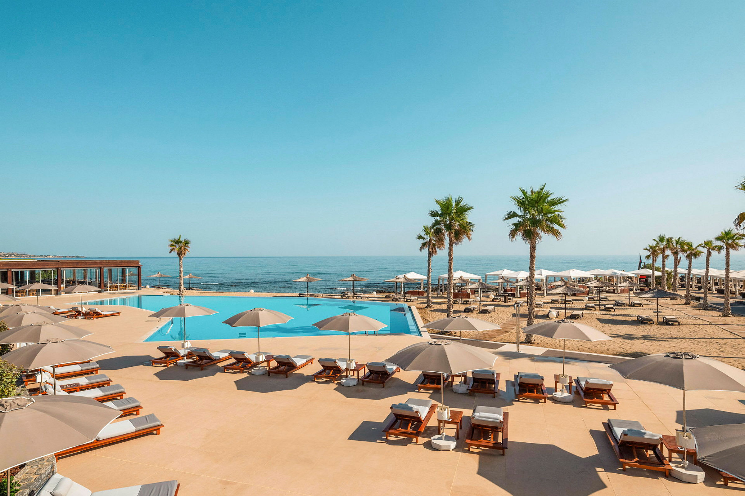 En pool med solstolar och parasoller vid stranden. (AI-genererad text)