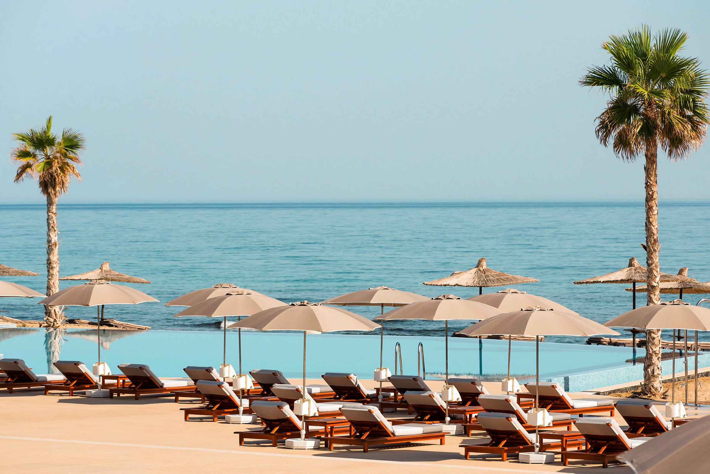 Solstolar och parasoller vid en infinitypool framför havet. (AI-genererad text)