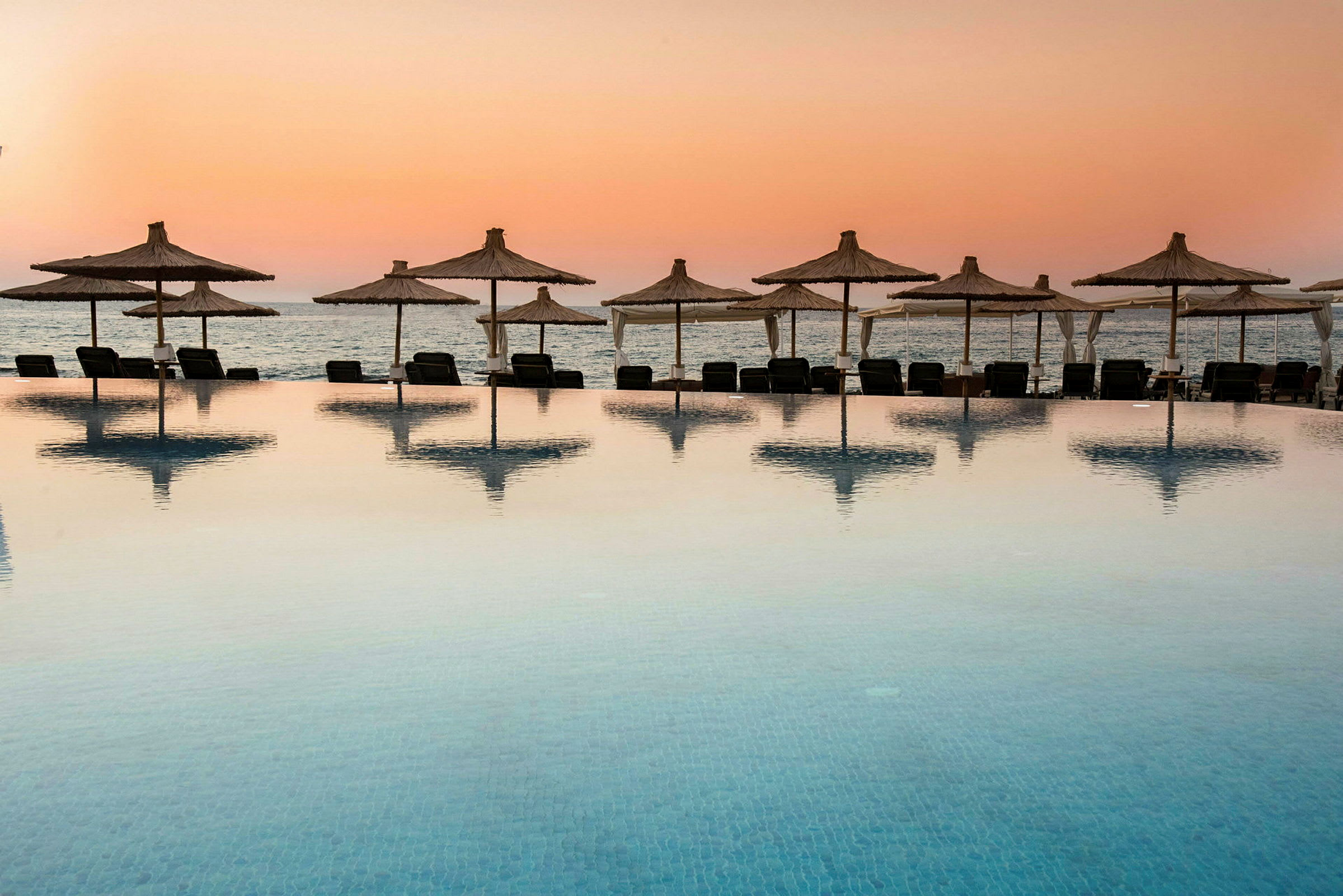 Pool med utsikt mot stranden vid solnedgång. (AI-genererad text)