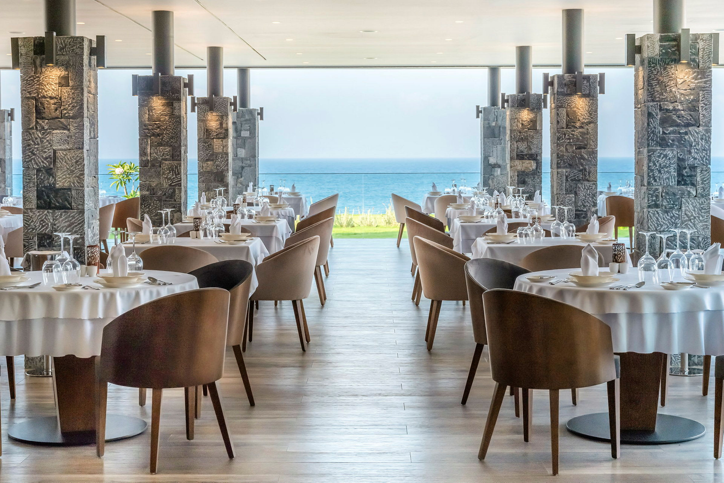 Restaurangbord med dukar och stolar, havsutsikt i bakgrunden. (AI-genererad text)