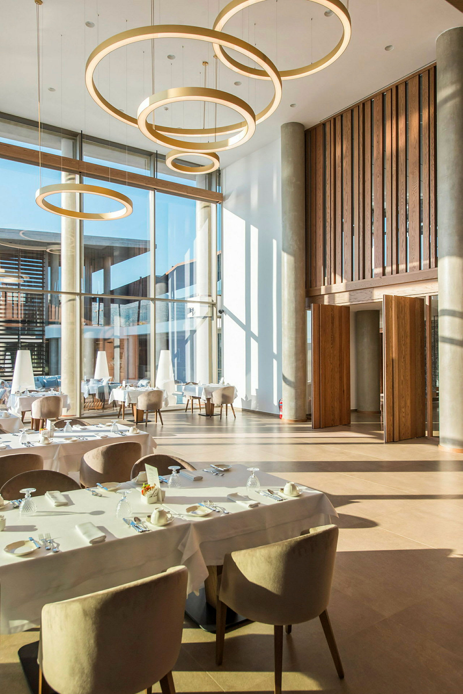 Interiör av en modern restaurang med stora fönster och hängande cirkelformade lampor. (AI-genererad text)