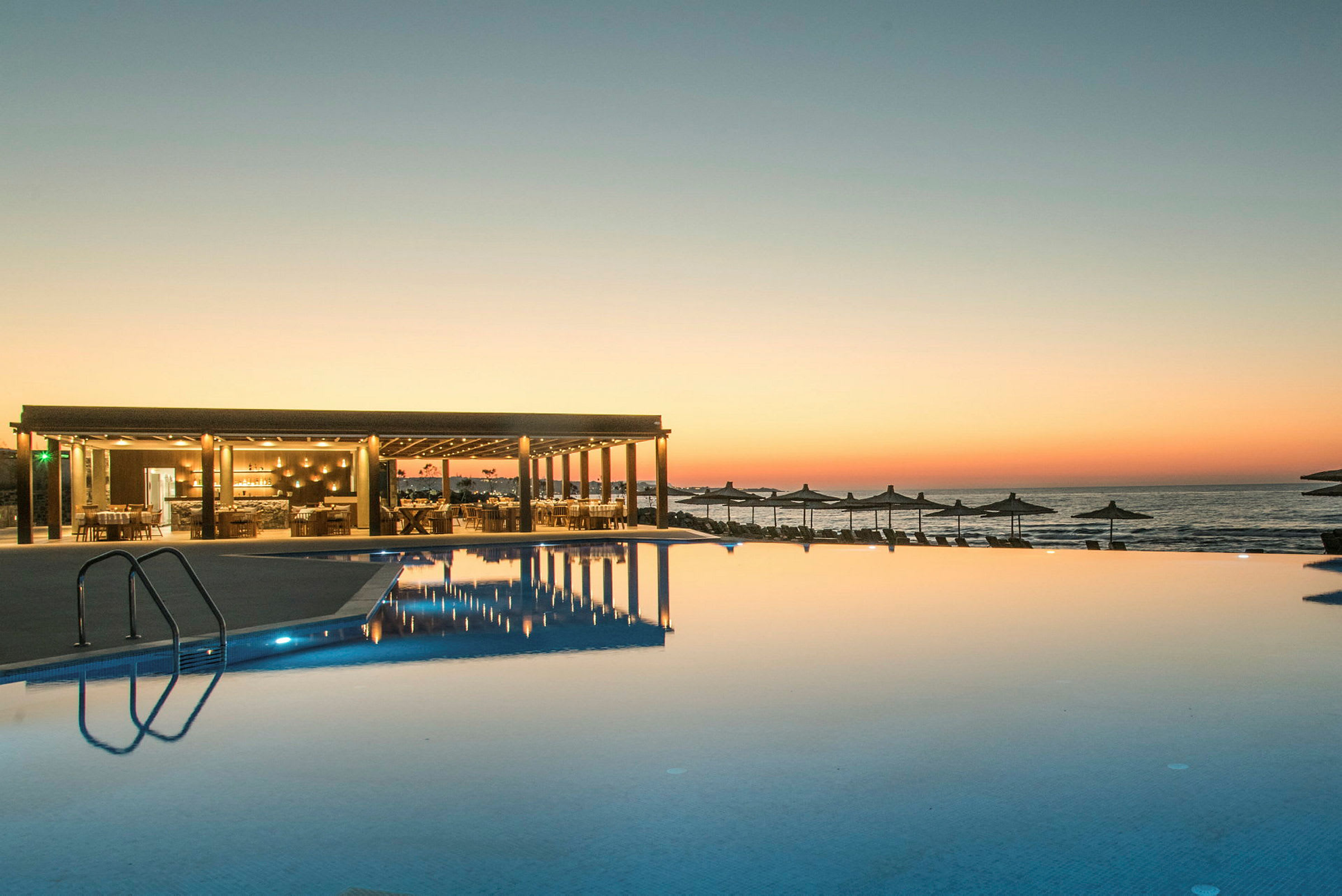 En infinitypool vid solnedgången med en restaurang till vänster och havet i bakgrunden. (AI-genererad text)