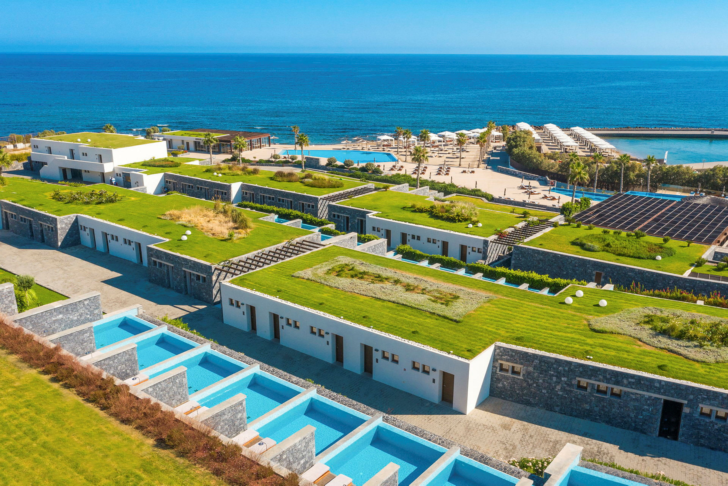 Bild av hotellområde vid havet med gröna tak och privata pooler. (AI-genererad text)