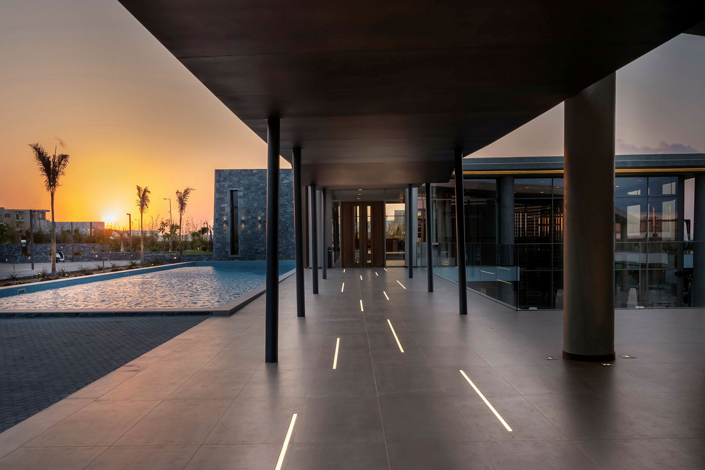 Modernt hotellområde vid solnedgången med pool och gångväg. (AI-genererad text)