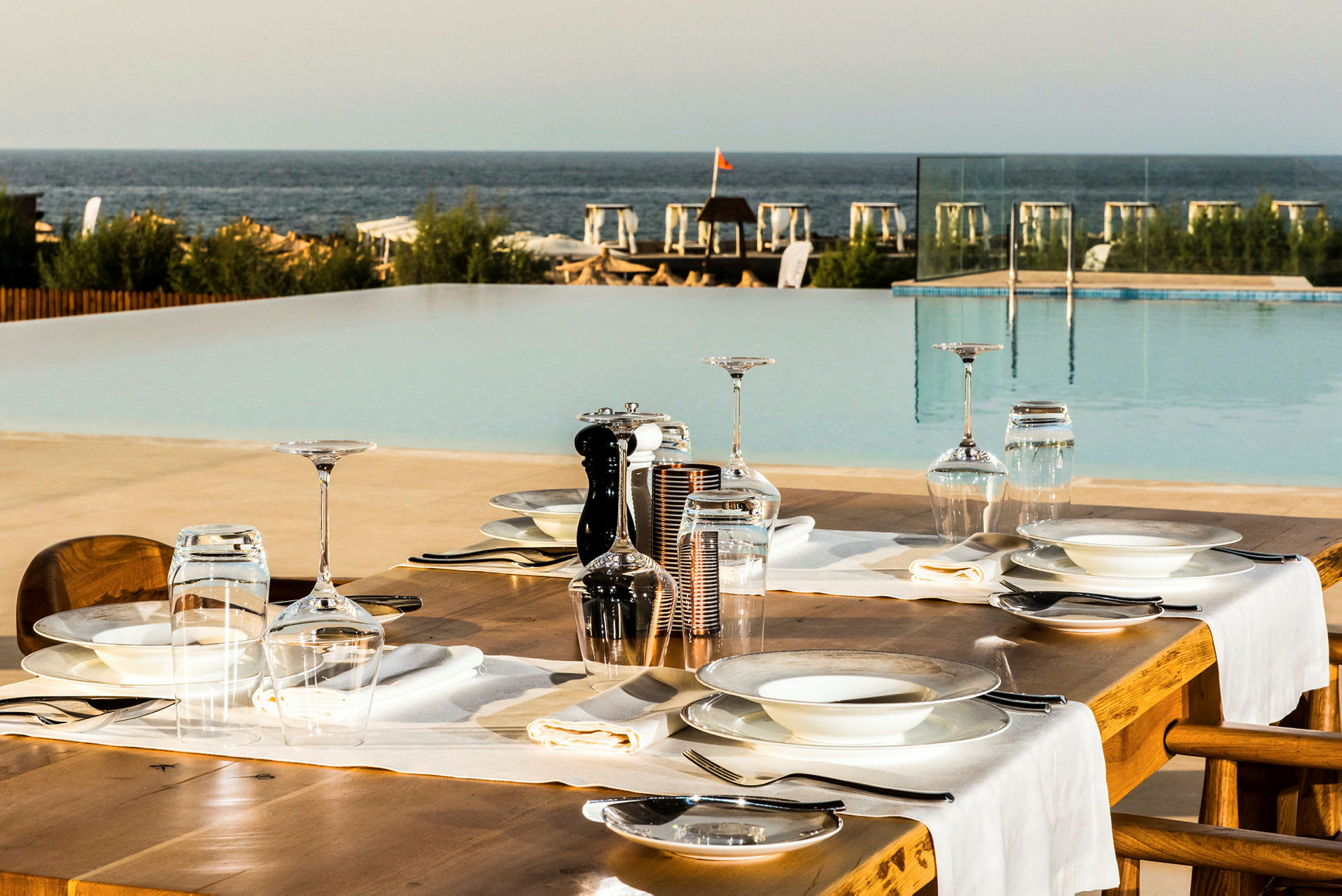 Ett dukat bord vid en pool med utsikt mot havet. (AI-genererad text)