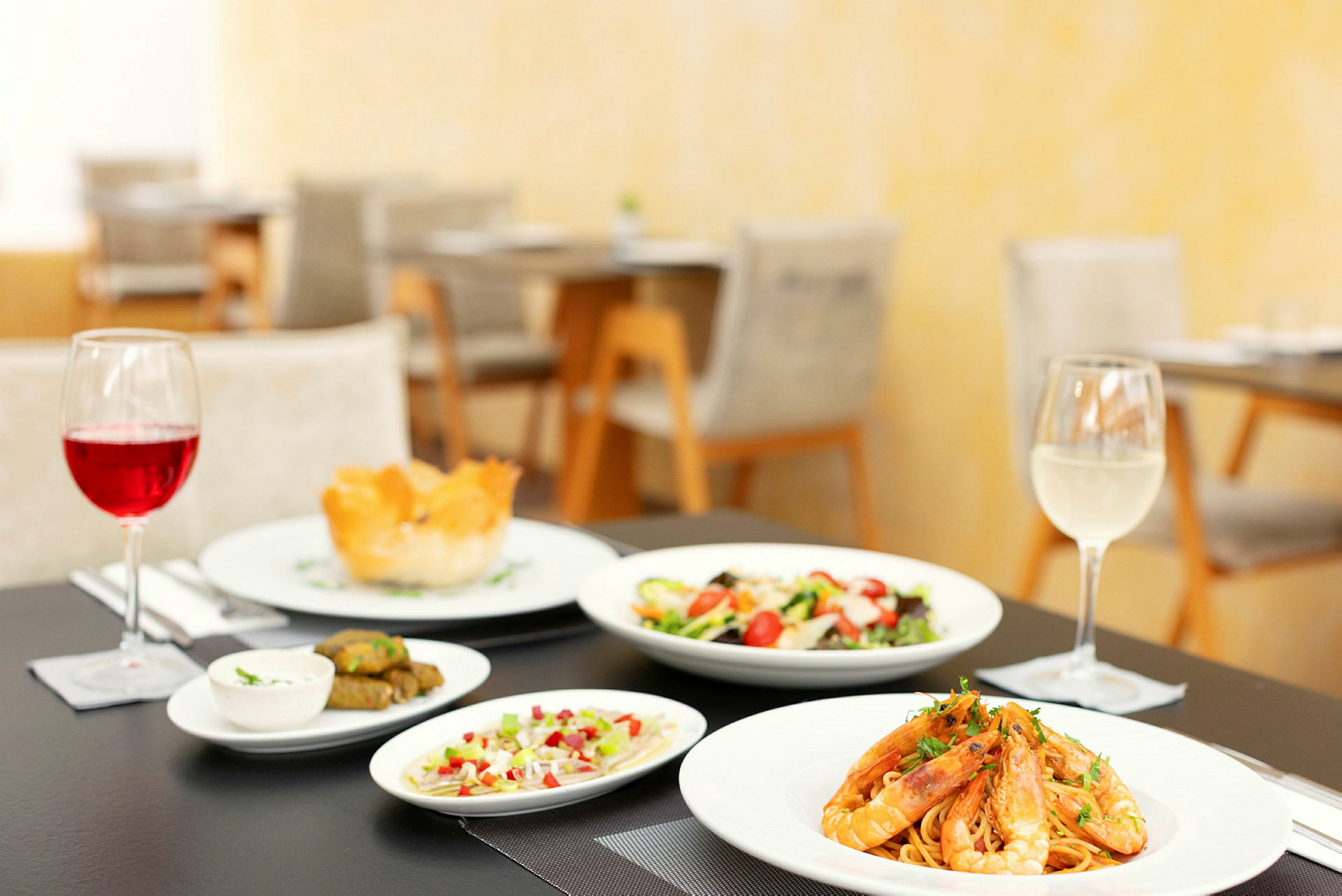 Bild av ett dukat bord med en måltid som inkluderar pasta med räkor, sallad, smårätter och två glas vin. (AI-genererad text)