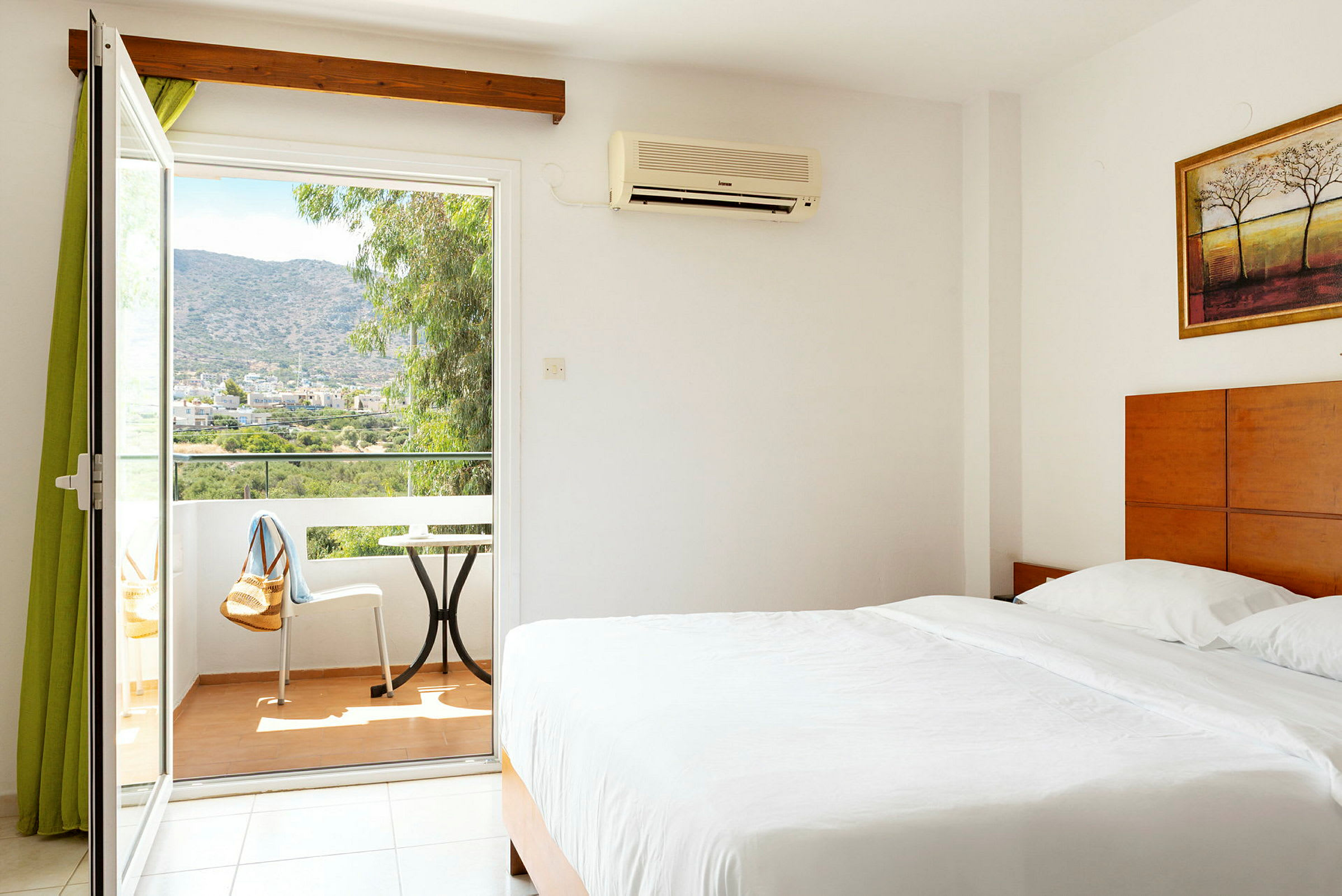 Ett hotellrum med en stor säng, vita sängkläder och ett öppet fönster med utsikt över en balkong och en bergig landskap. (AI-genererad text)
