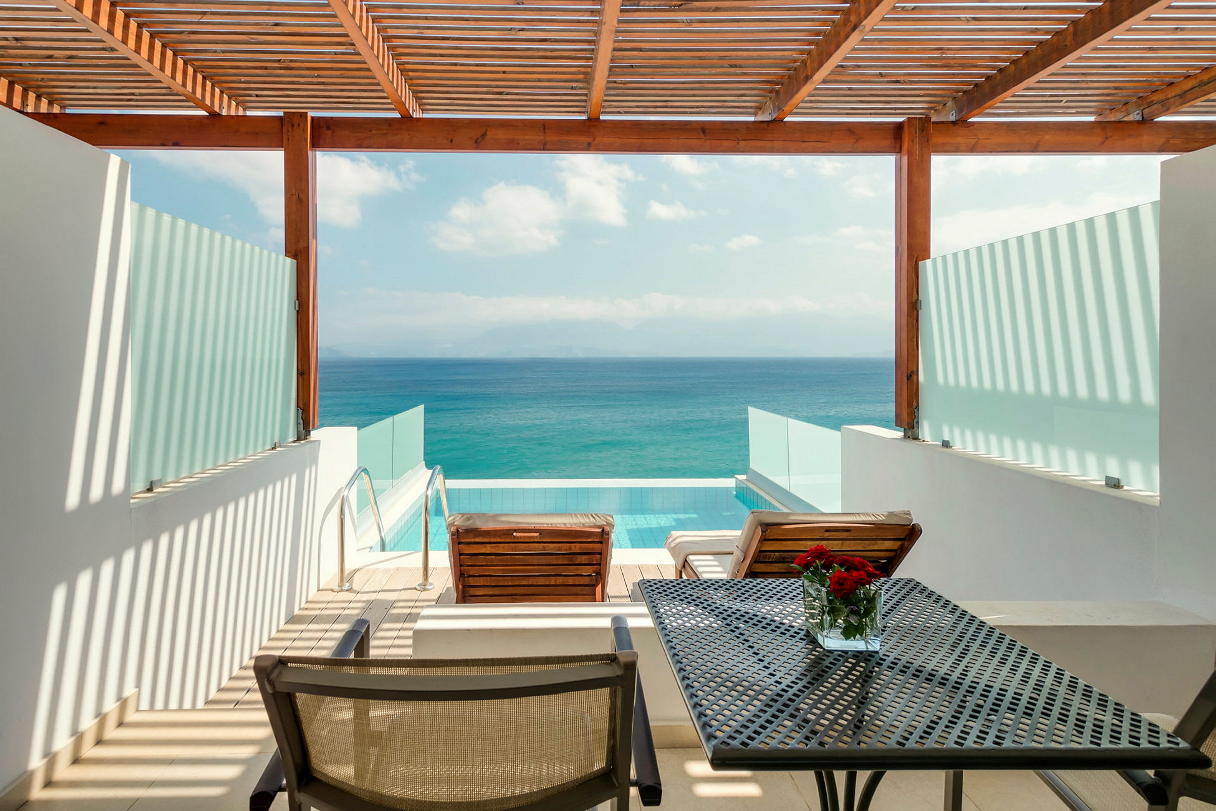 Utsikt över en terrass med två solstolar, ett bord och en privat pool, med havet i bakgrunden. (AI-genererad text)
