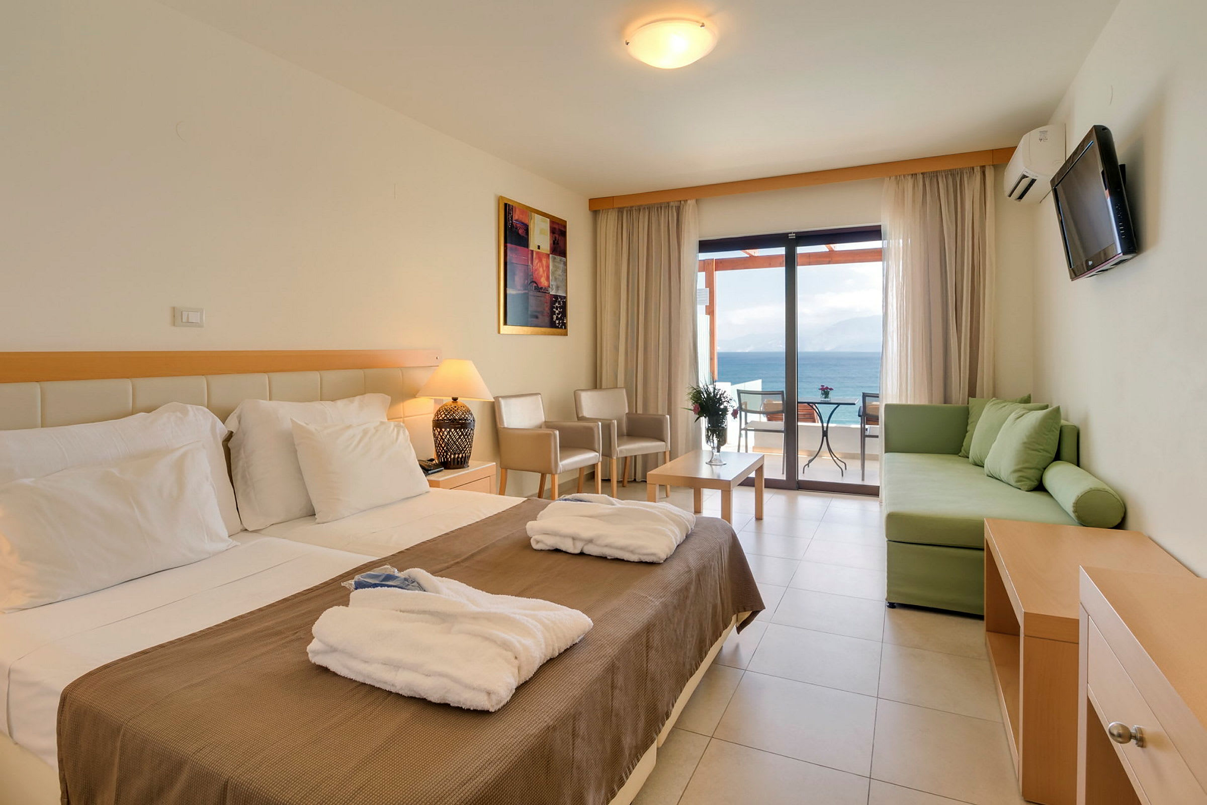 Hotellrum med säng, soffa och möblerad balkong med havsutsikt. (AI-genererad text)