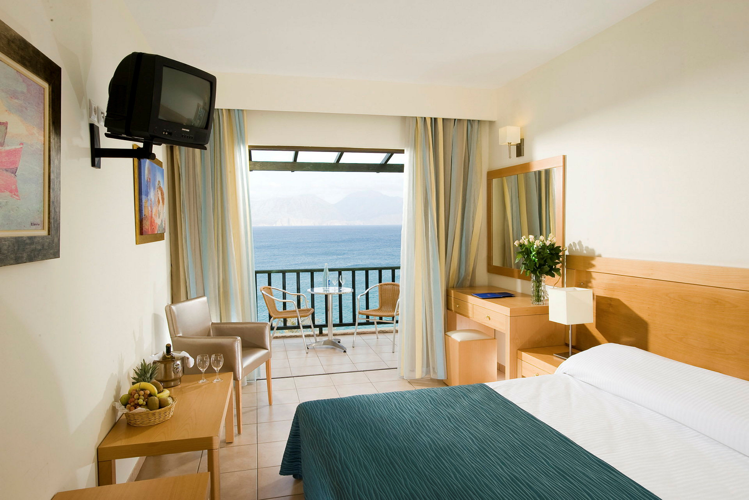 Ett hotellrum med en säng, ett skrivbord, stolar och en balkong som erbjuder utsikt över havet. (AI-genererad text)