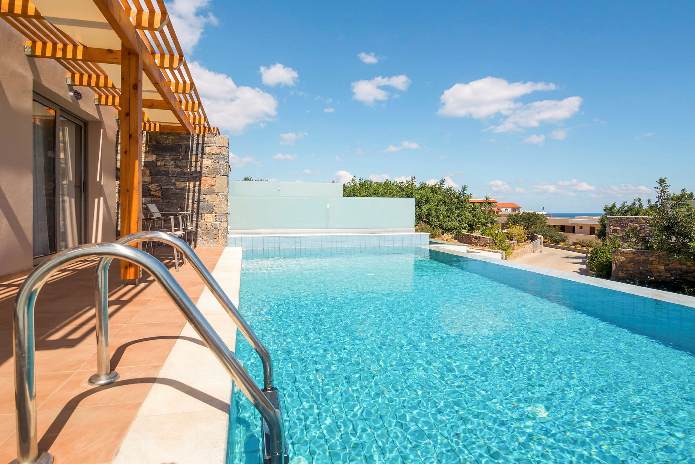En infinitypool vid ett hus med solsken och utsikt över grönska och himmel. (AI-genererad text)