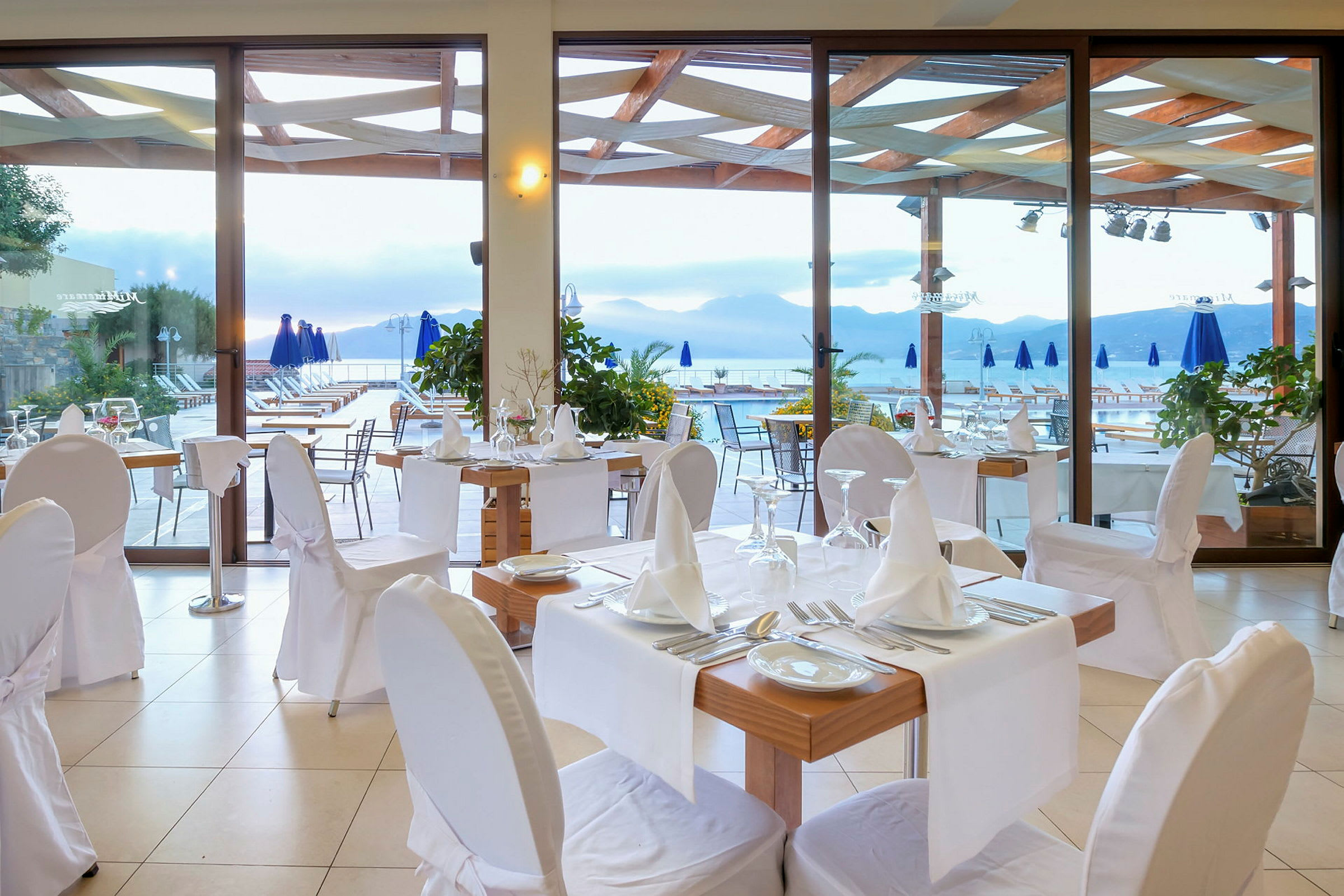 En restaurang med dukade bord och stolar, vid en terrass med utsikt över ett berg och vatten. (AI-genererad text)