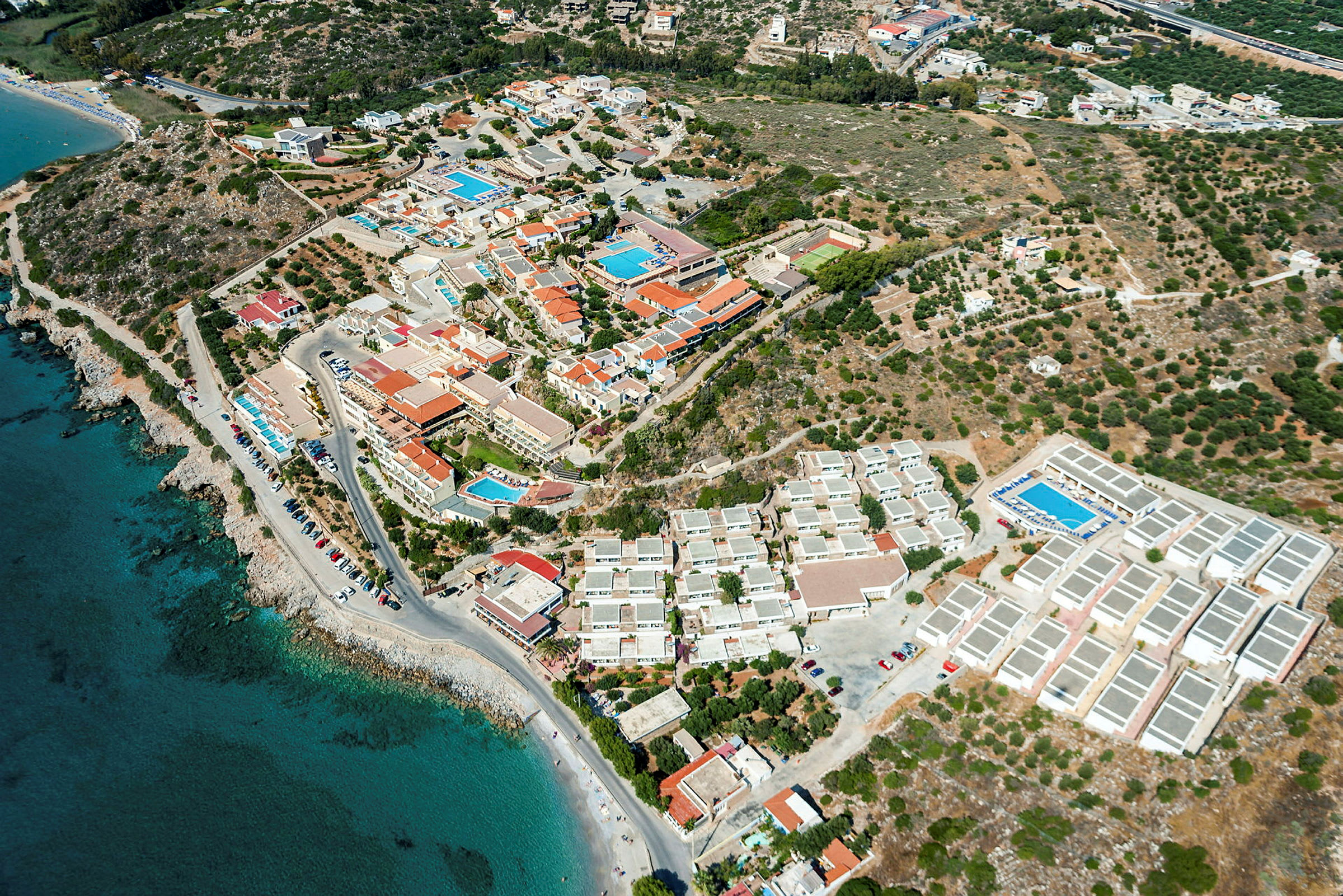 Luftbild av en kustnära ort med byggnader, hotell och simbassänger. (AI-genererad text)