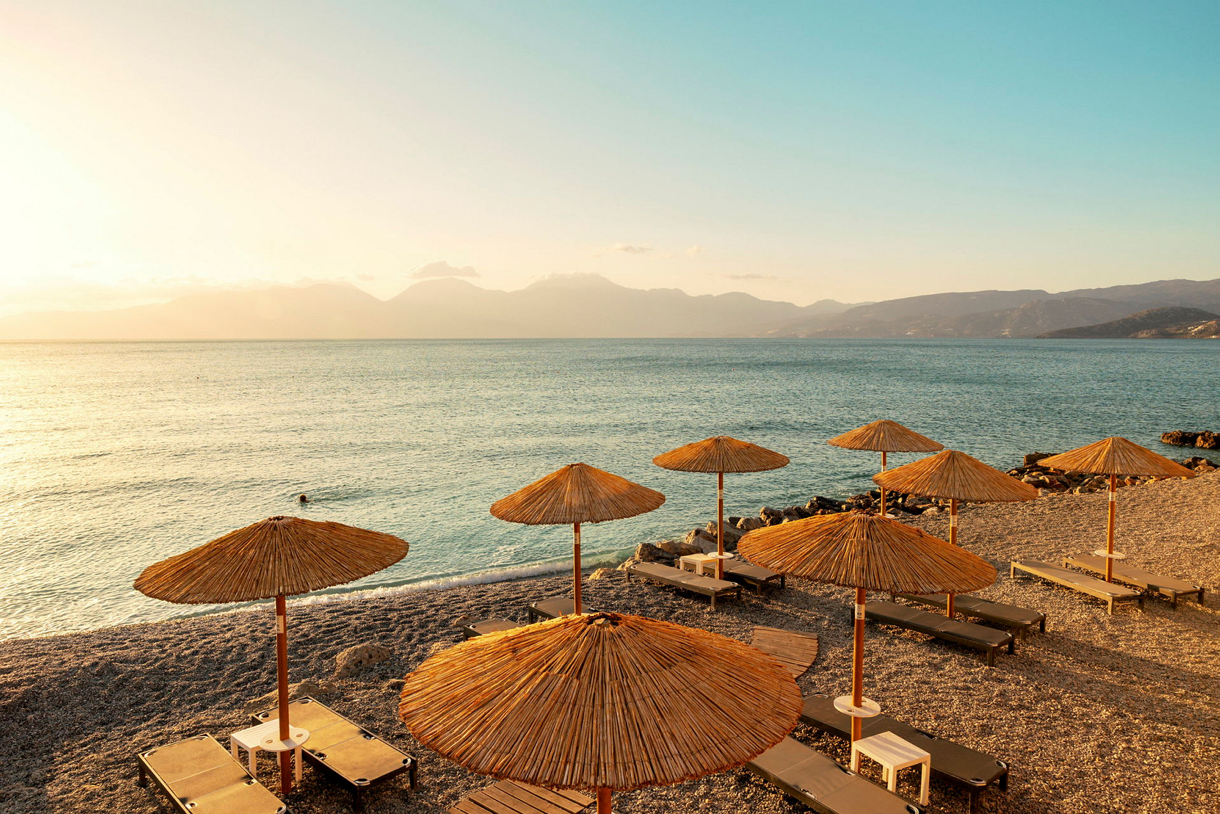 Strand med solstolar och parasoller samt utsikt över havet vid solnedgång. (AI-genererad text)