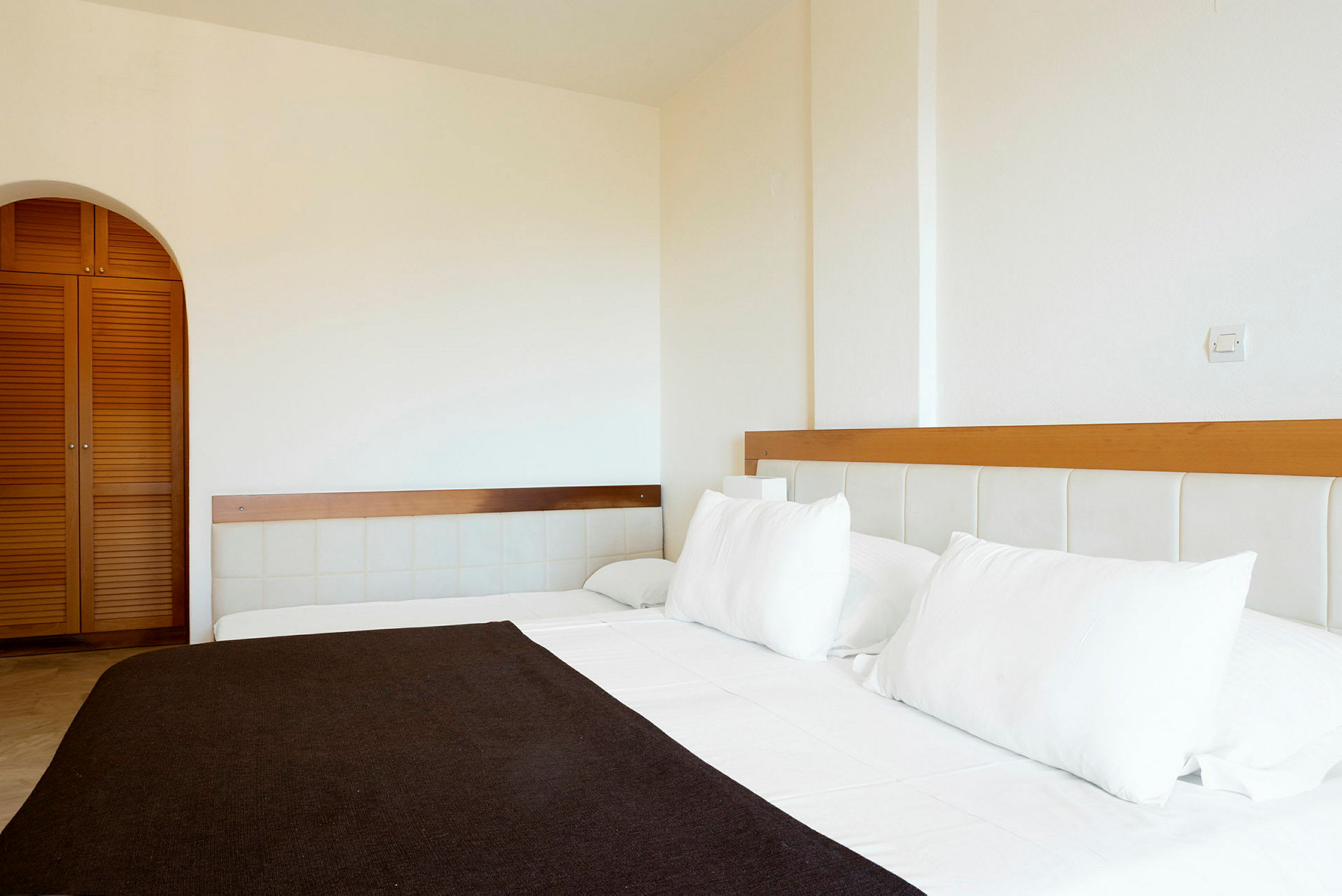 Ett hotellrum med en bäddad säng med vita lakan och kuddar. En garderob med trädörrar syns i bakgrunden. (AI-genererad text)