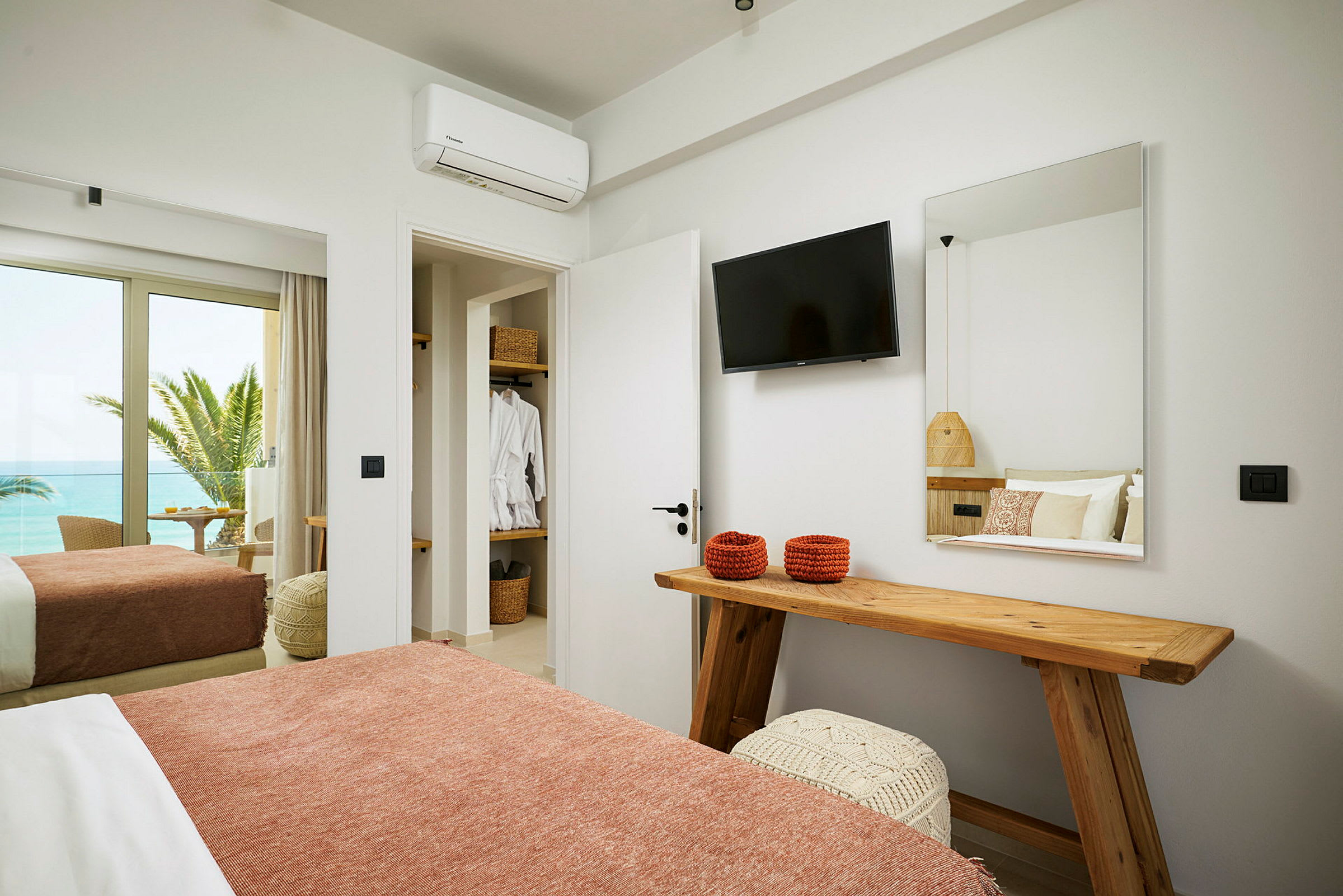 Hotellrum med säng, TV, spegel och utsikt mot havet. (AI-genererad text)