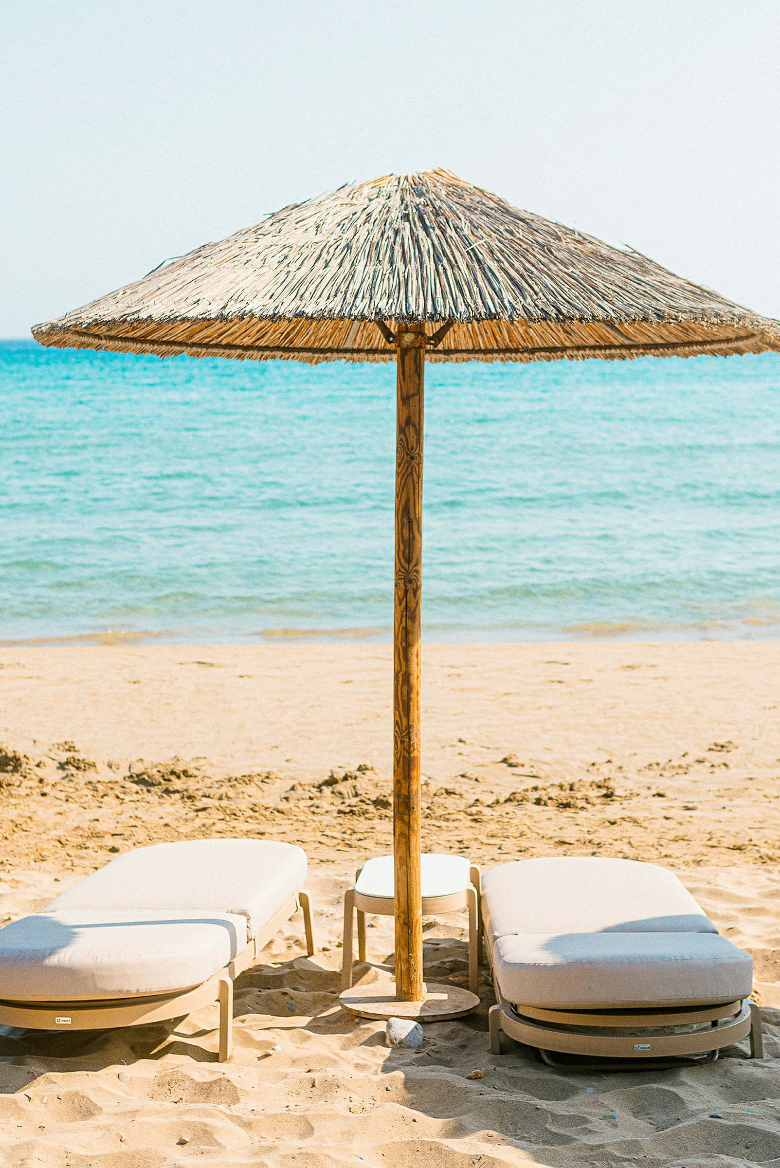 Strand med två solstolar och en parasoll av strå. (AI-genererad text)