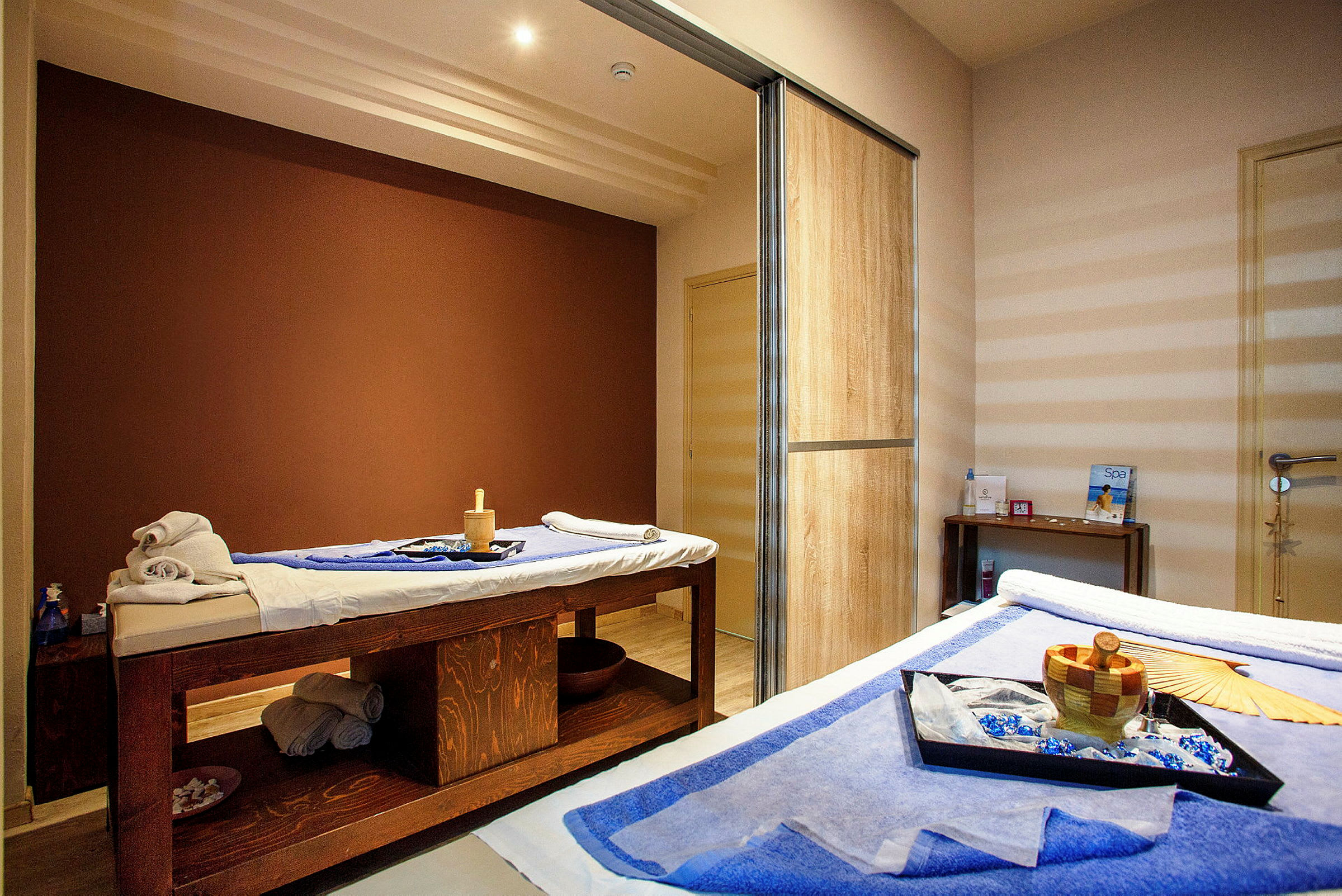 Ett rum med terapeutiska behandlingsbord täckta med handdukar och spa tillbehör. (AI-genererad text)